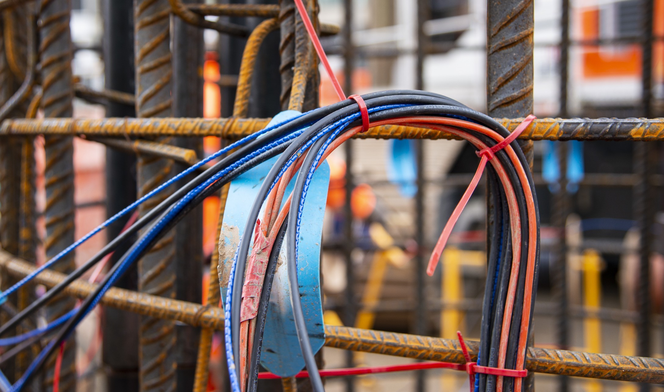 Electrical wiring installation on steel rebar at construction site Coiled electrical cables tied to rusted metal rebar at a construction site.