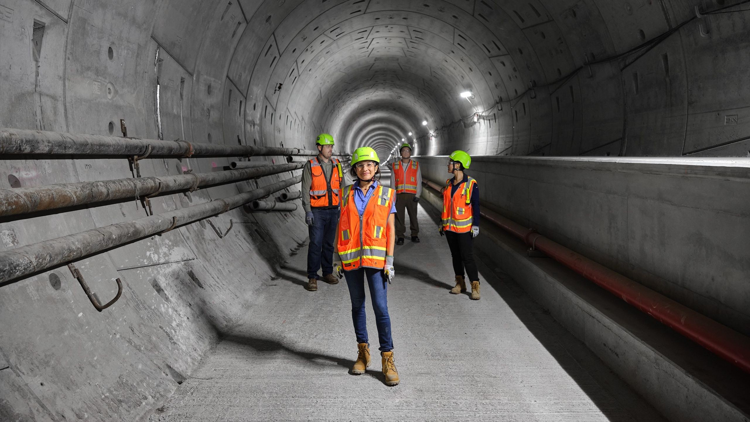 Construction Workers in Tunnel with Safety Gear Construction workers wearing safety gear stand inside a large underground tunnel.
