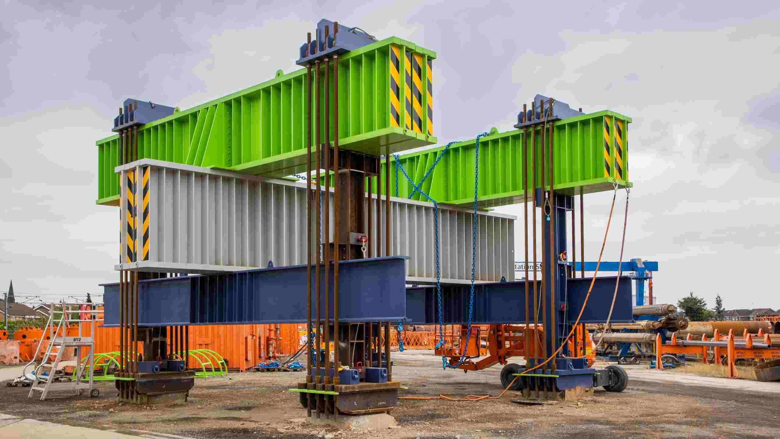 Construction site with large steel beams and girders in green, gray, and blue colors.