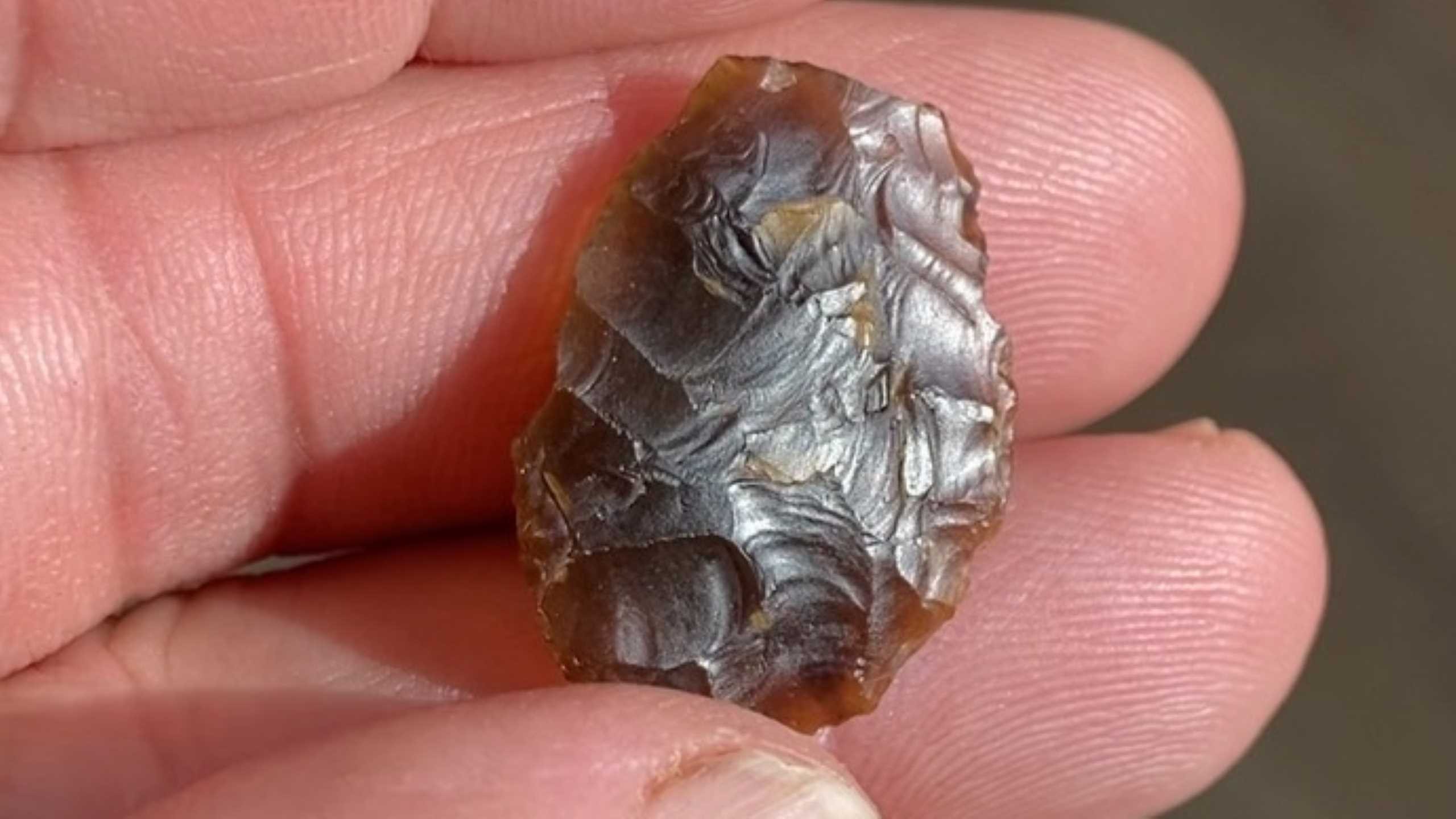 Hand holding a small, translucent brown flint tool with detailed flaked edges.