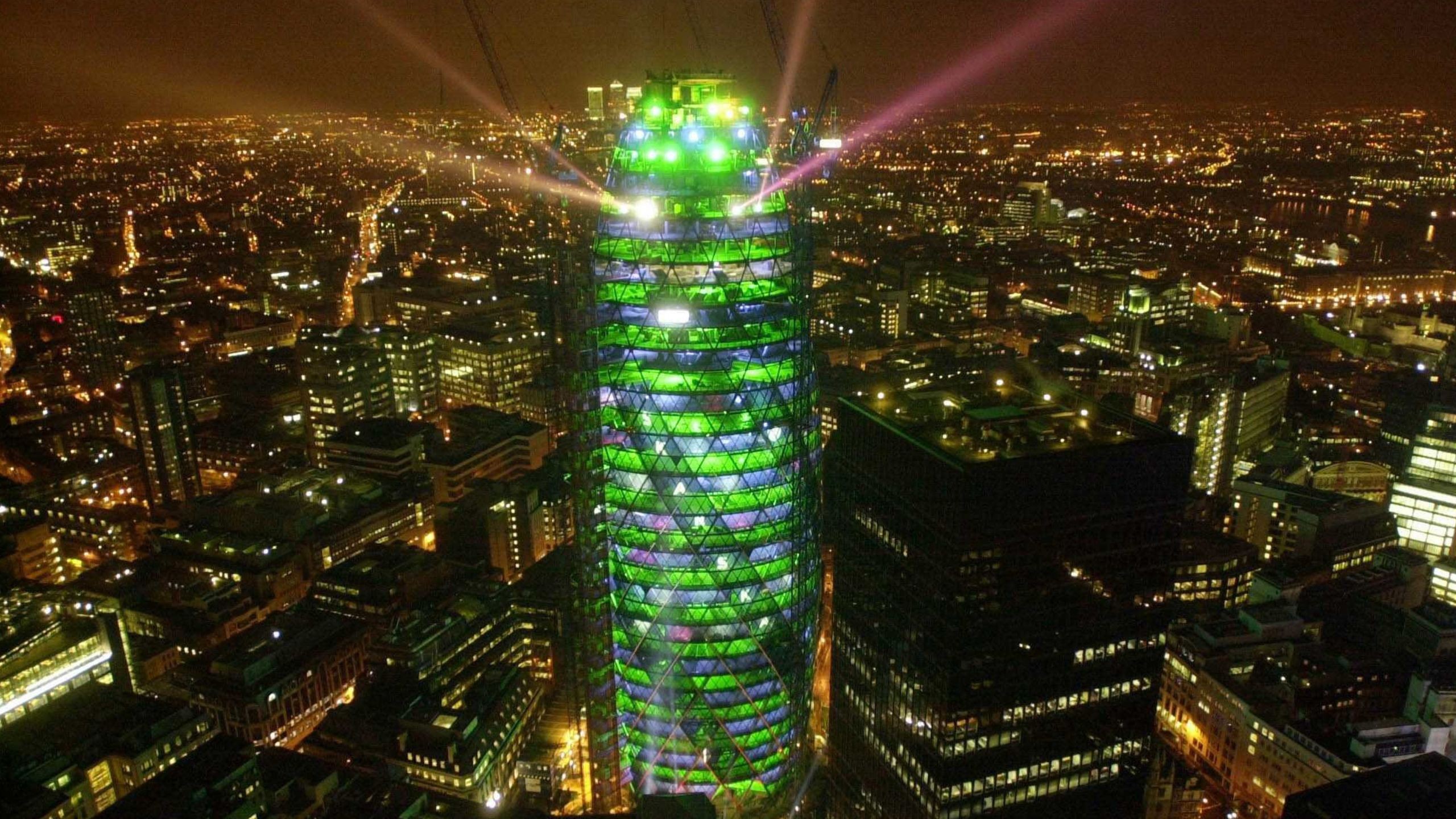 Night cityscape with a tall, illuminated skyscraper featuring green and purple lights.