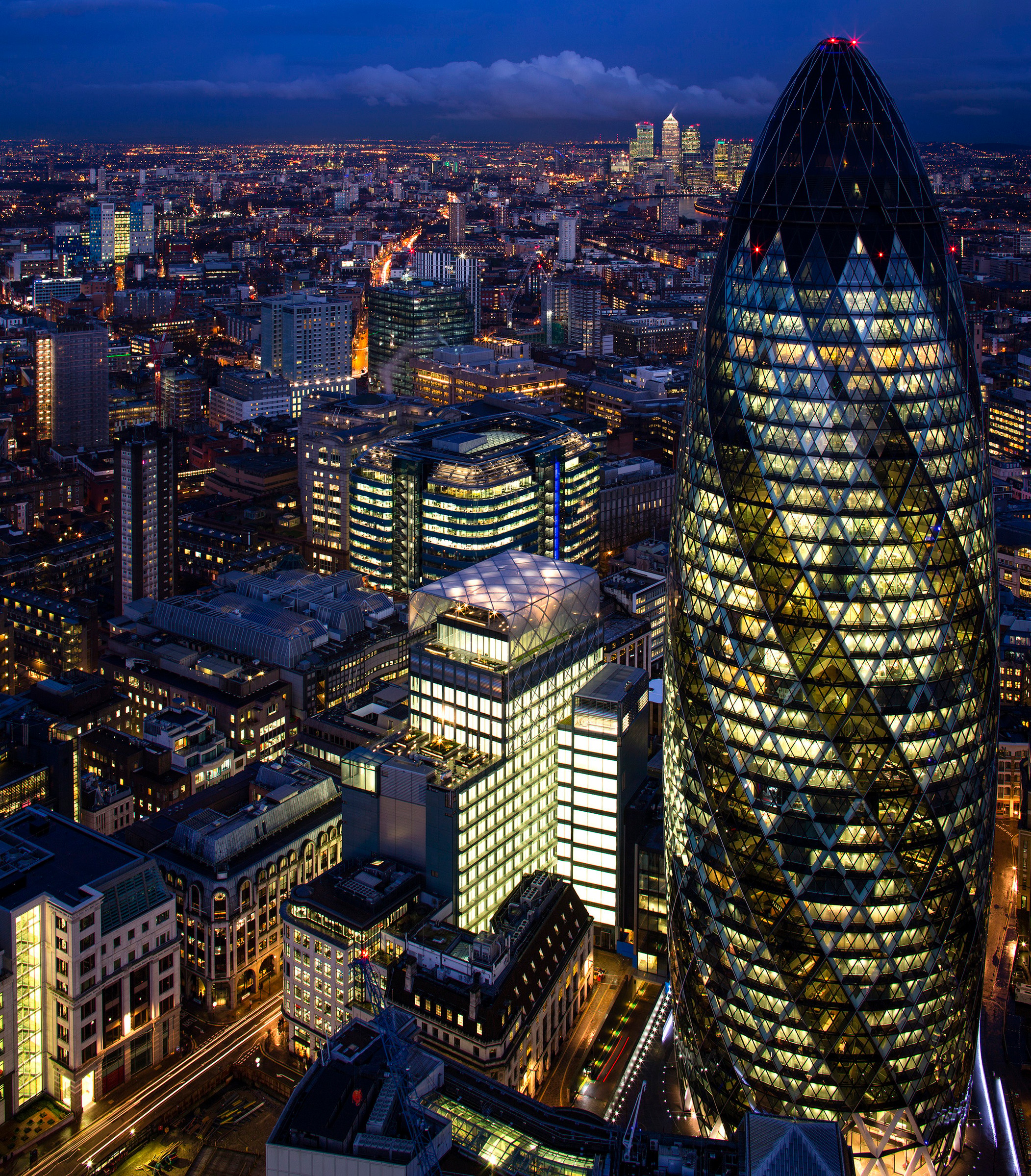 Night view of London's cityscape featuring the illuminated Gherkin building amidst skyscrapers.