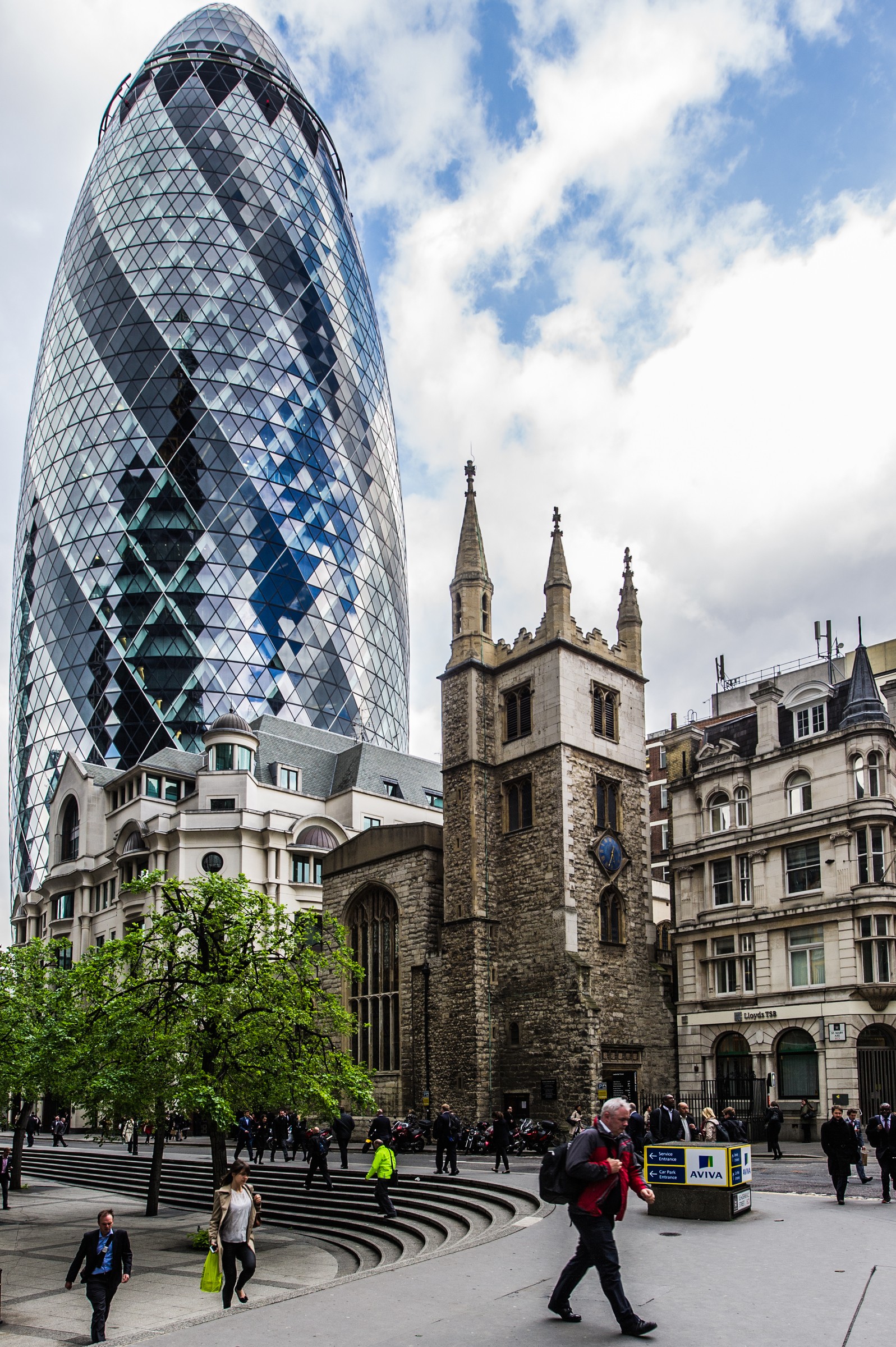 Modern skyscraper, The Gherkin, towers beside historic church, contrasting old and new architecture.