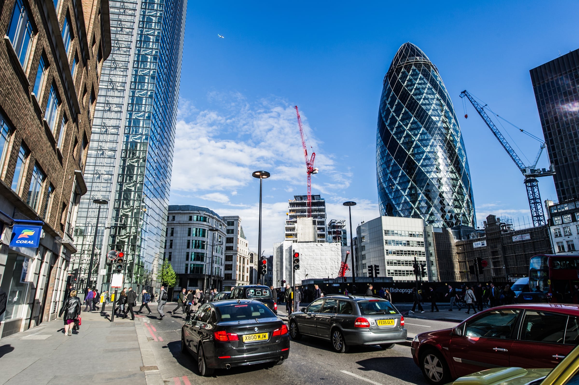 London street scene with traffic, pedestrians, and the iconic Gherkin building under a blue sky.