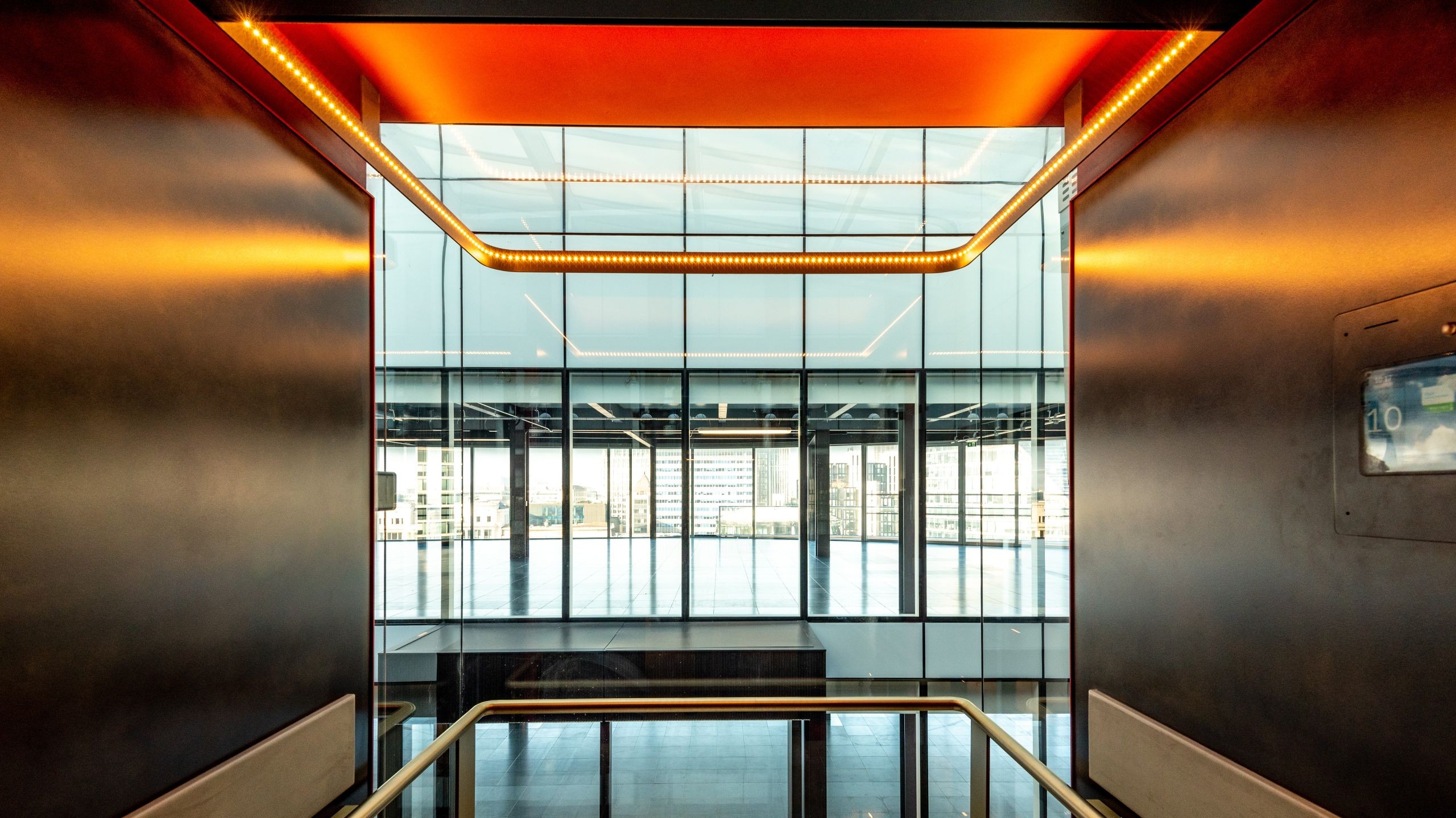 60 London Wall Modern glass elevator interior with orange ceiling lights and city view outside.