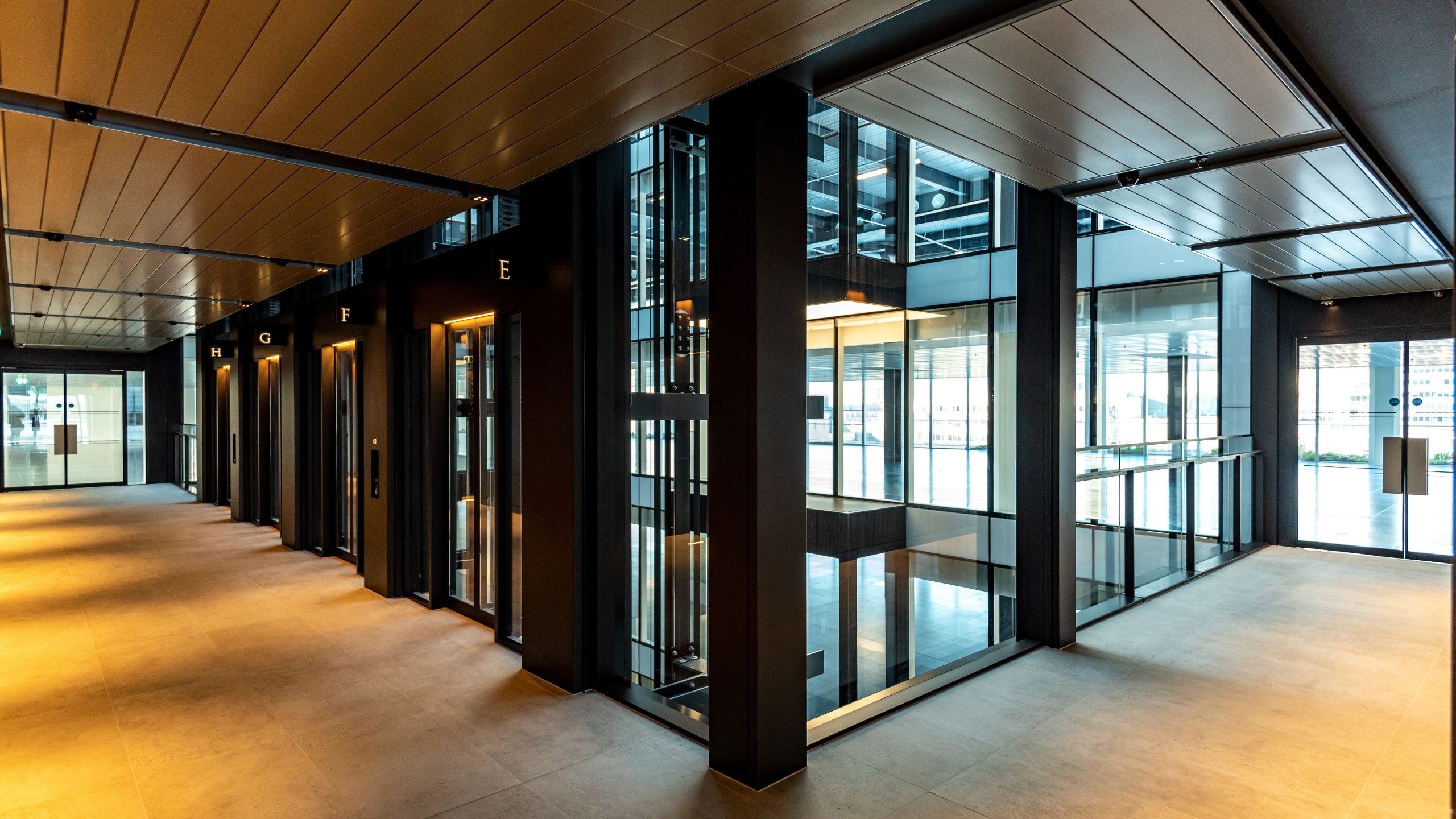 Modern office lobby with glass elevators and warm lighting on tiled floors.
