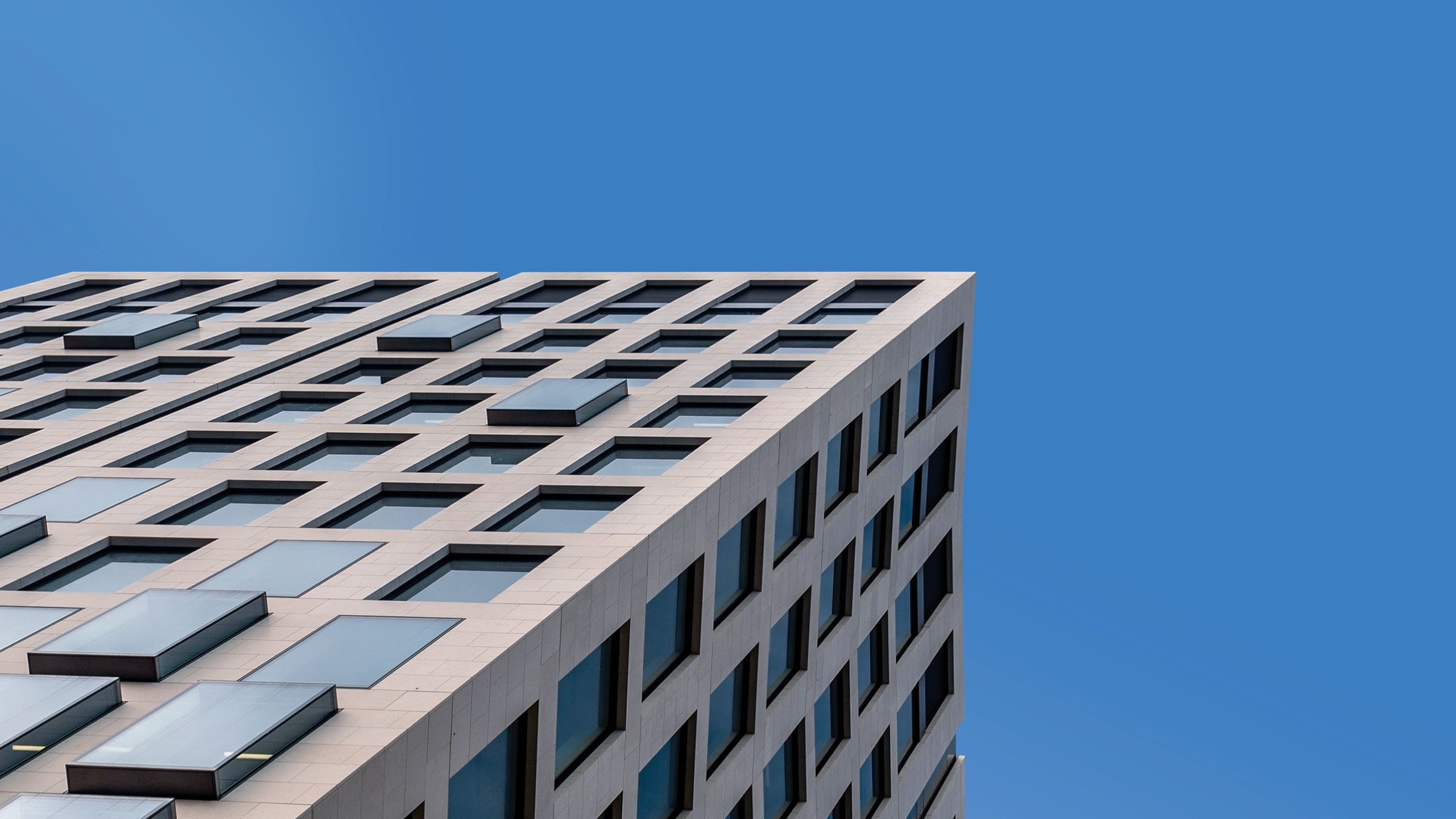 Modern office building facade with clear blue sky background Modern high-rise building with numerous windows against a clear blue sky.