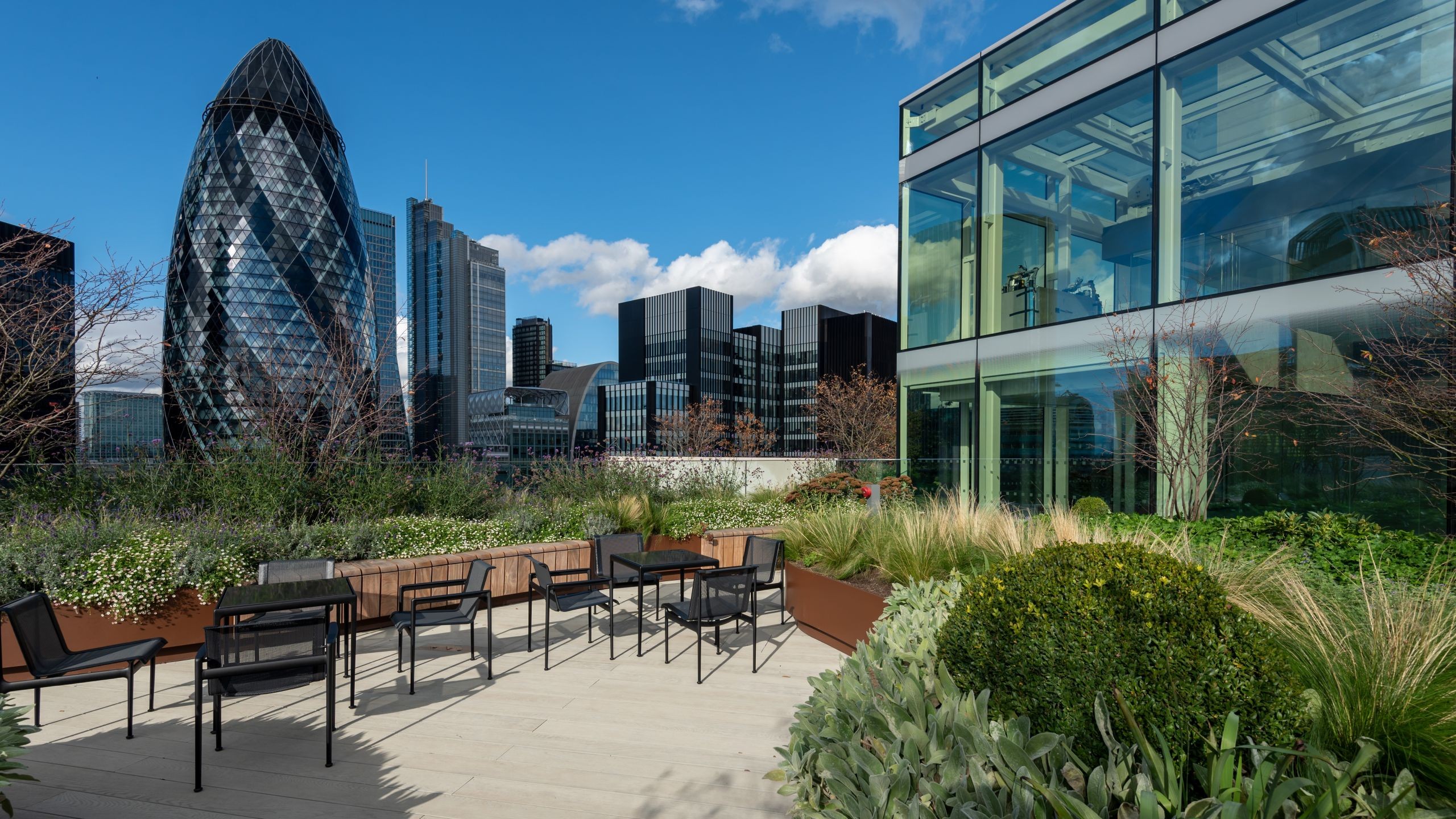 Modern rooftop terrace with seating and plants overlooking London city skyline.