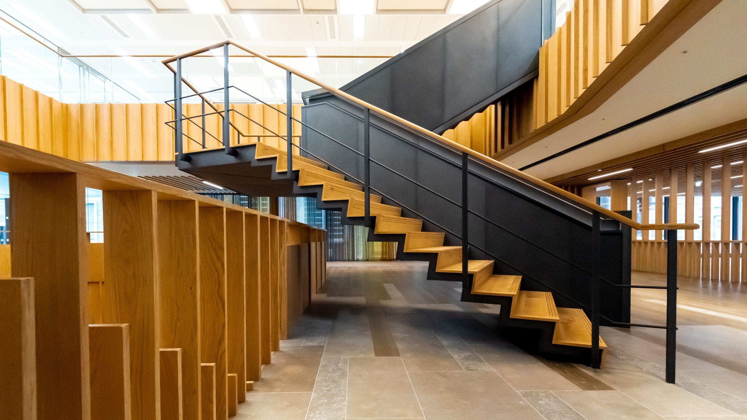 Modern wooden and black metal staircase in a spacious, well-lit office interior.