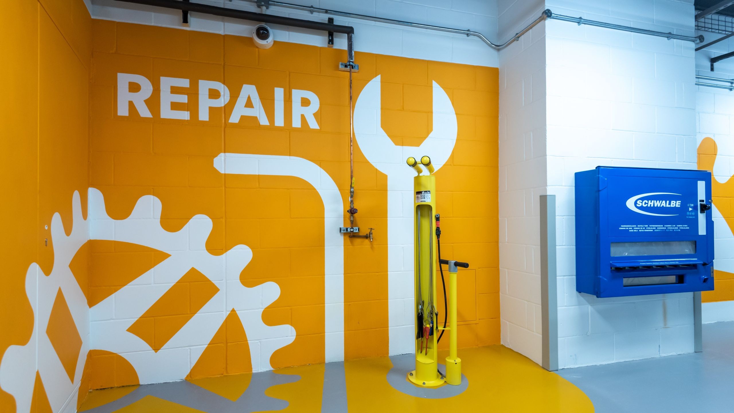 Bright yellow bike repair station with tools and Schwalbe tire dispenser on white wall.