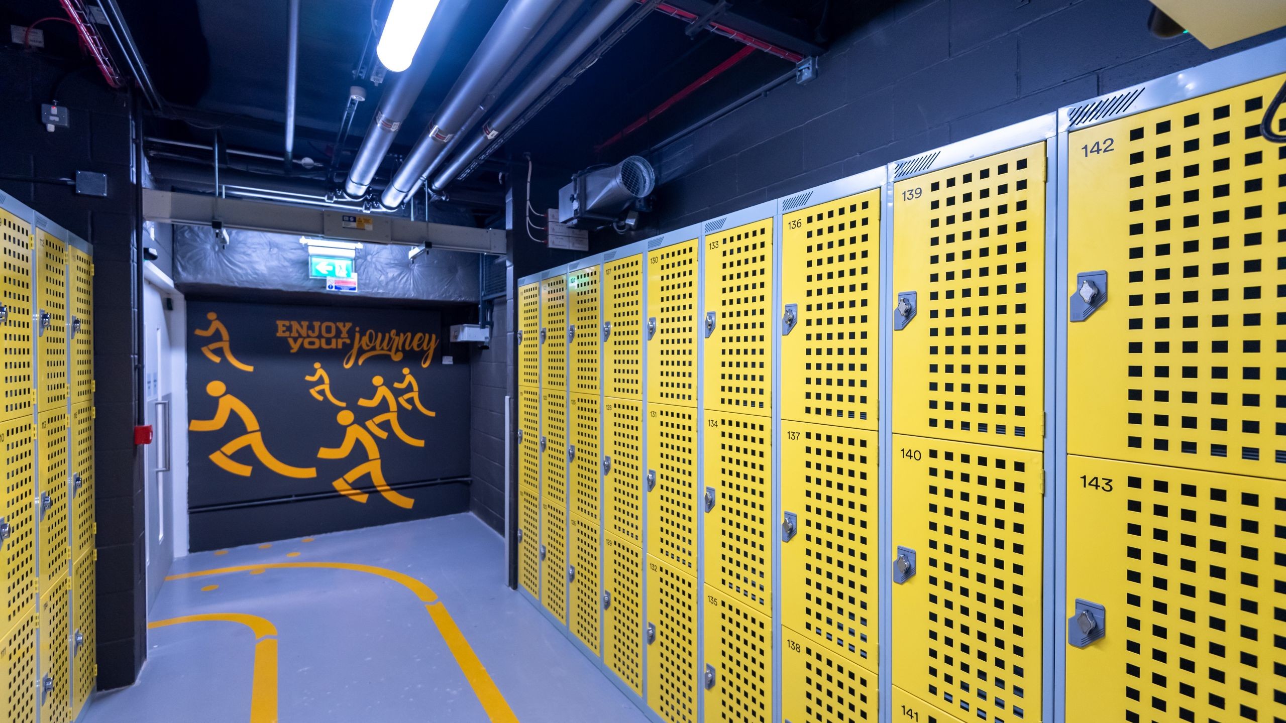 Bright yellow lockers in a modern gym locker room with motivational wall art.