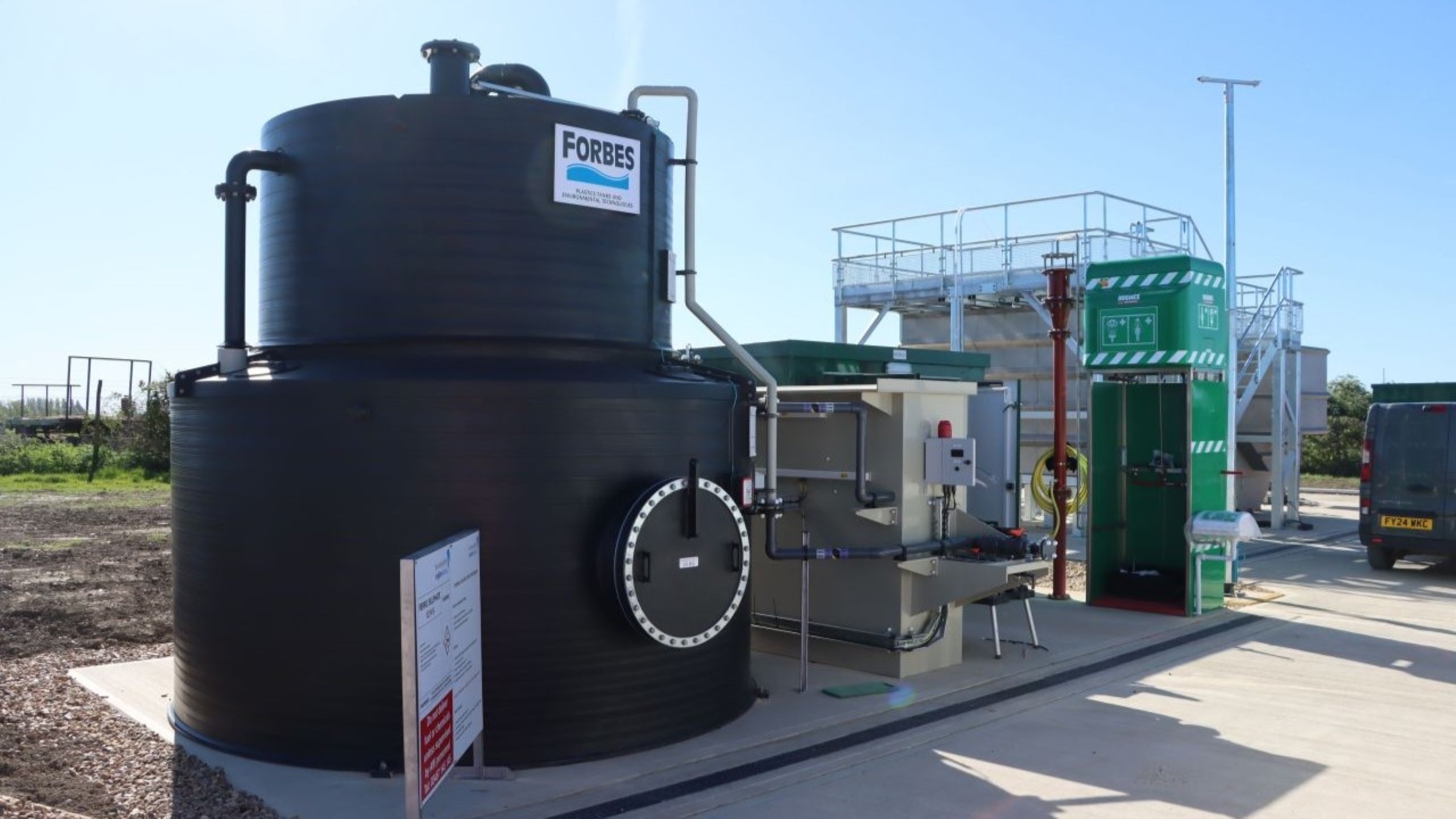 Large black industrial water tank with equipment and clear blue sky in the background.