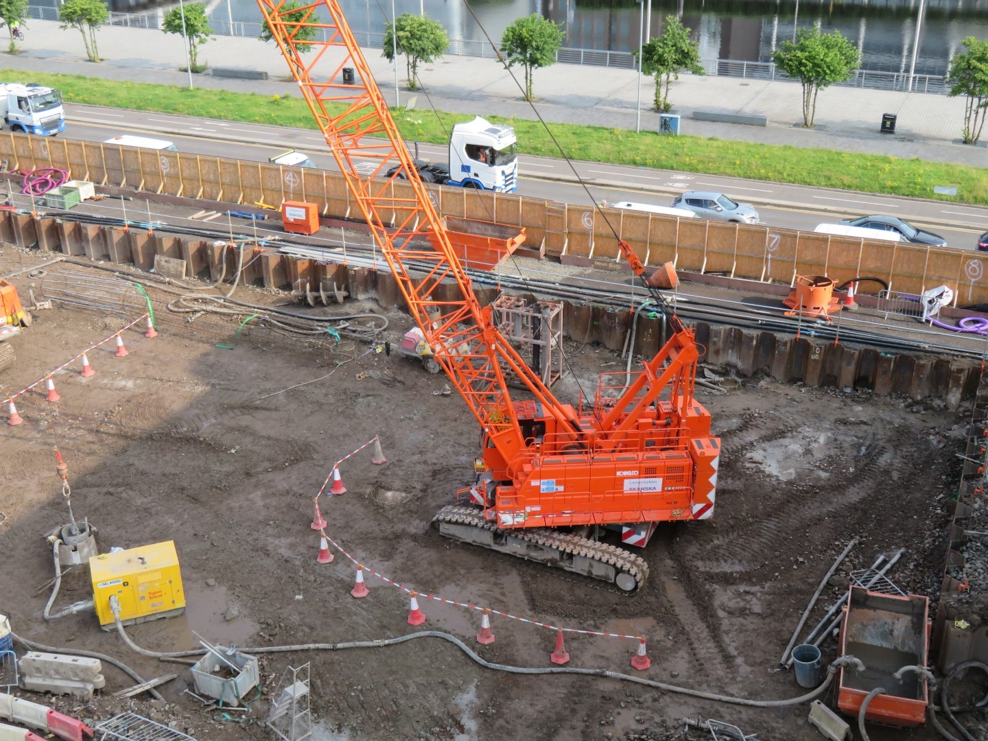 Construction site with an orange crawler crane surrounded by traffic cones and equipment.
