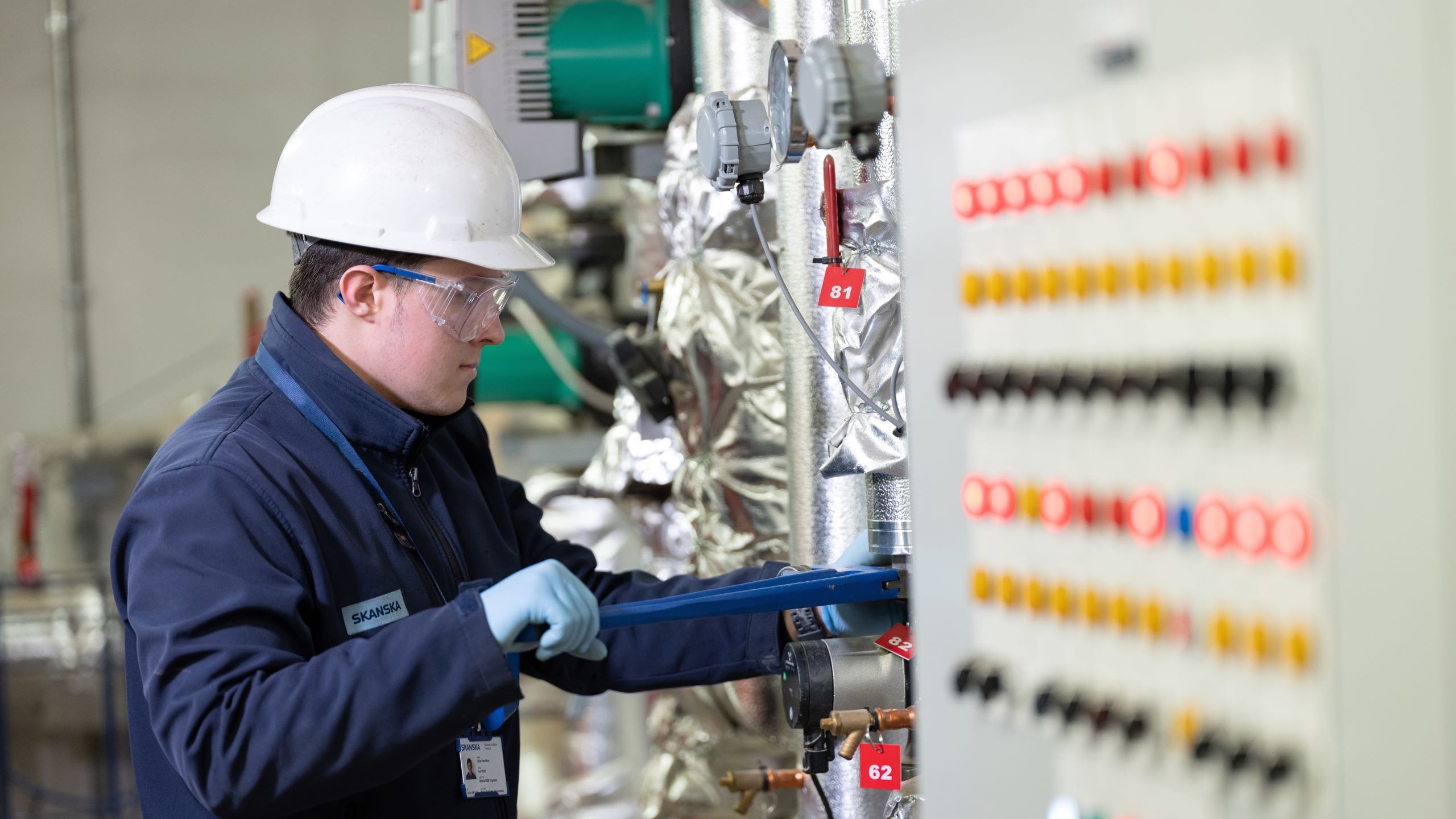 Facilities maintenance Technician in hard hat and gloves using wrench on industrial machinery gauges.