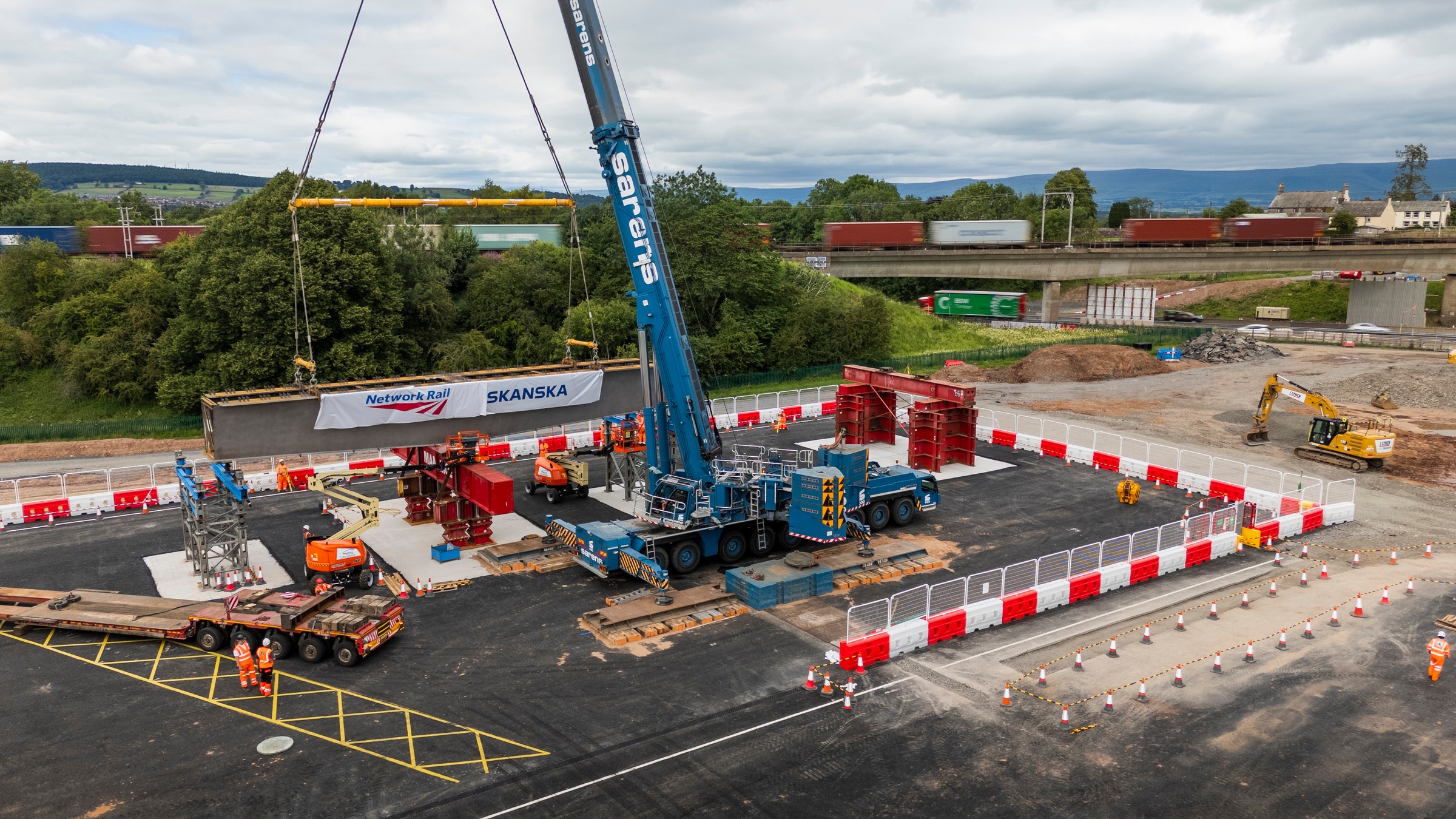 Railway Bridge Construction by Skanska - Project Site View Construction site with crane lifting bridge beam, featuring Skanska and Network Rail signage.