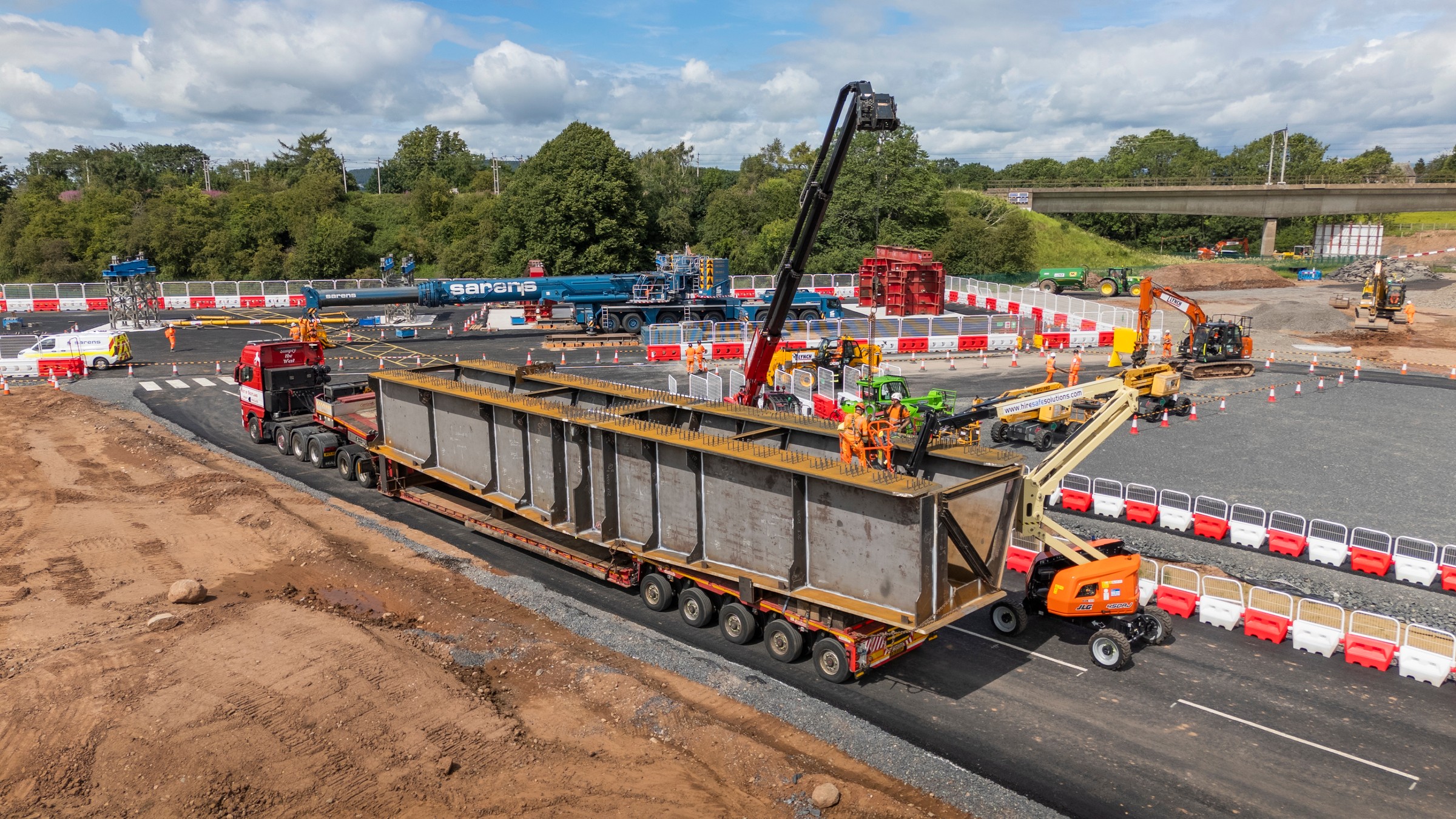 Heavy Equipment Transport at Construction Site Construction site with workers and cranes installing a large steel structure on a multi-axle truck.