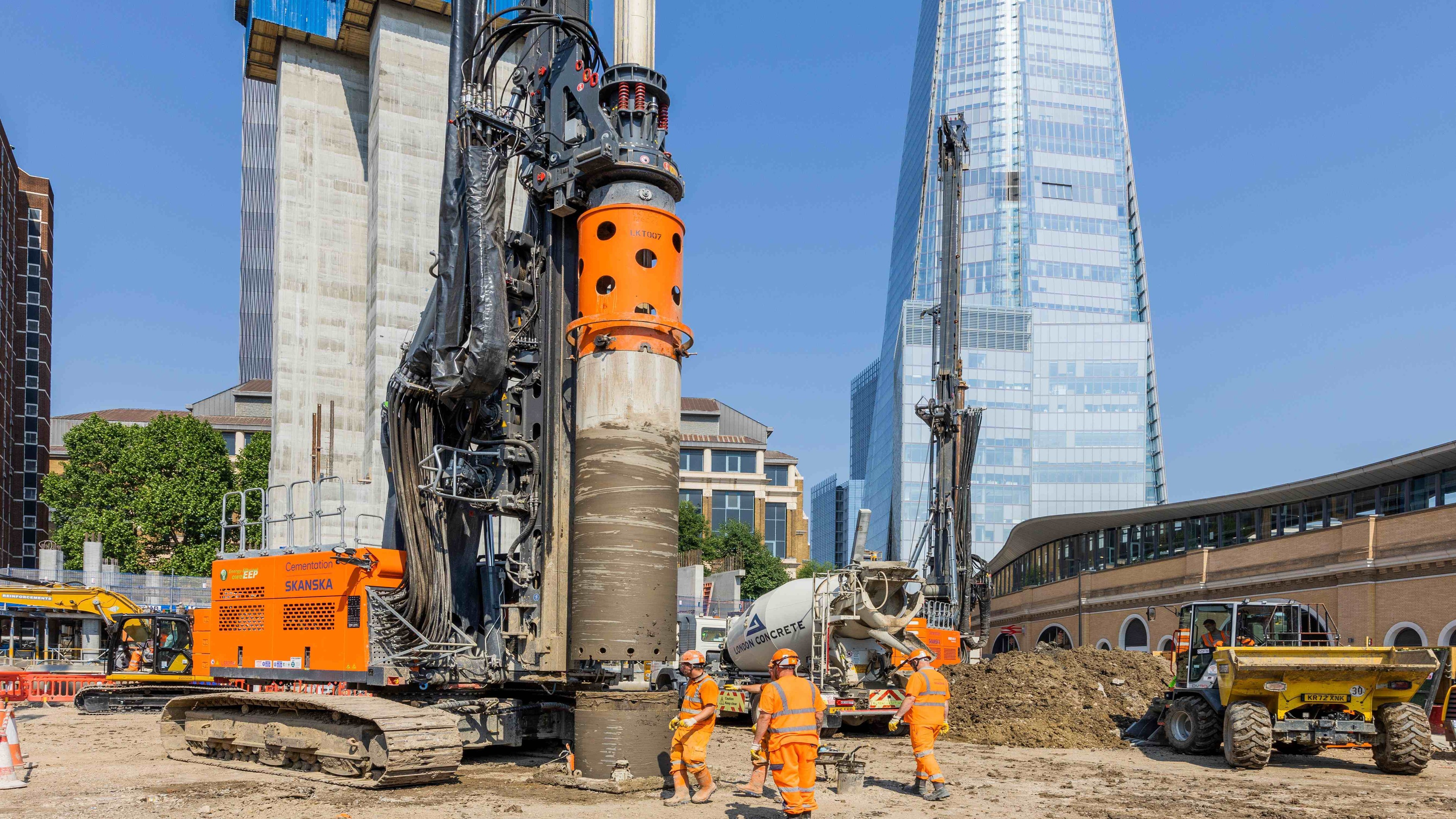 Construction workers operate a large drilling machine at an urban building site.