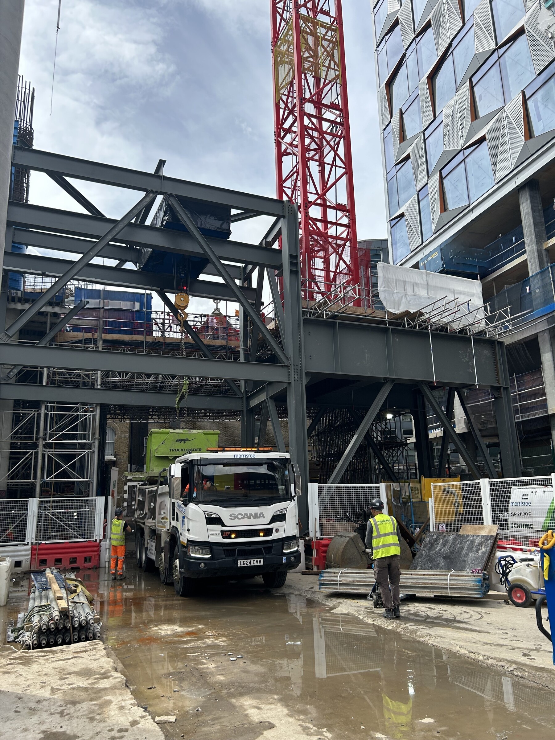 Construction site with a Scania truck, crane, steel structures, and workers in safety gear.
