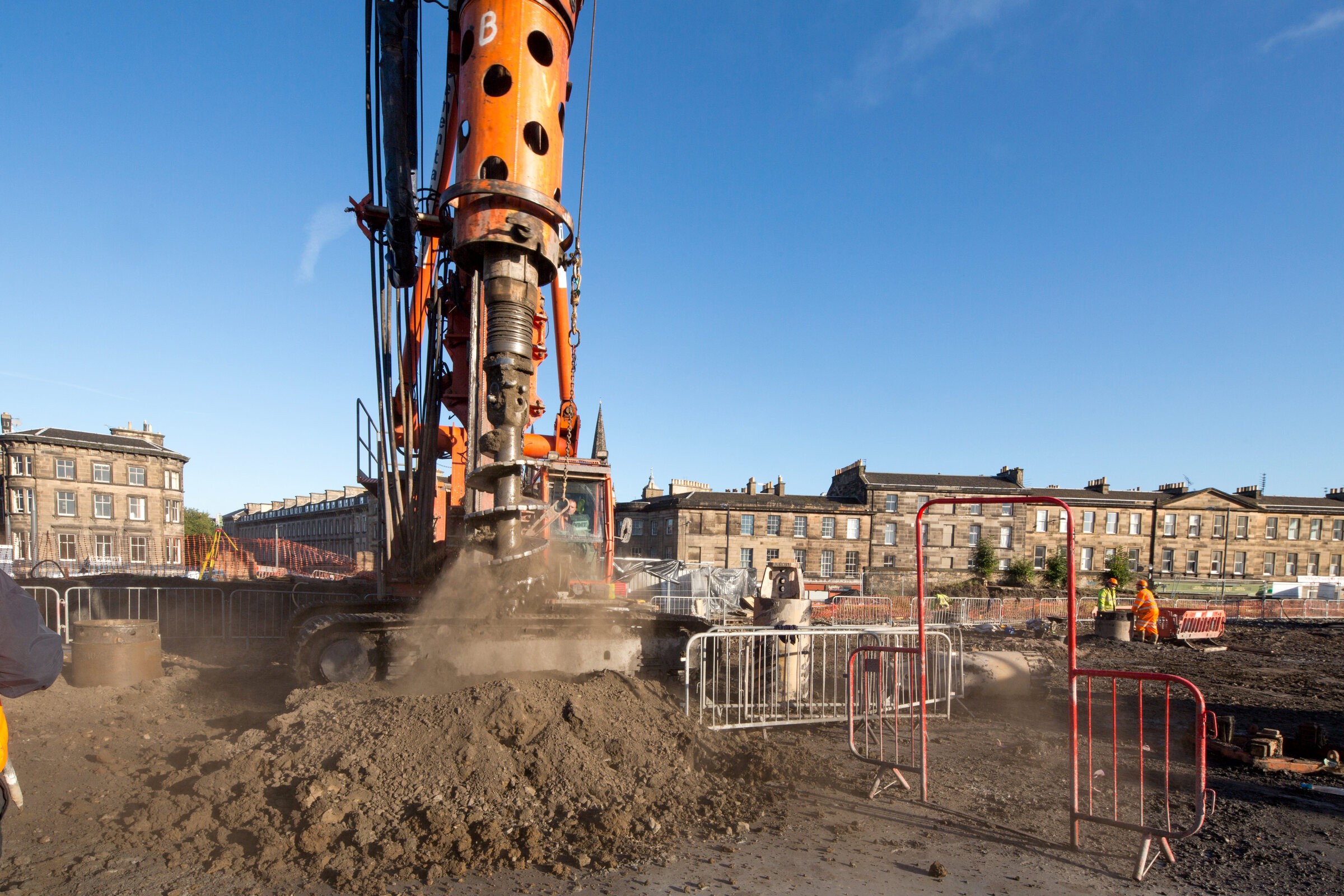 Construction Site with Heavy Machinery in Urban Area Large drilling machine at a construction site, surrounded by safety barriers and workers.