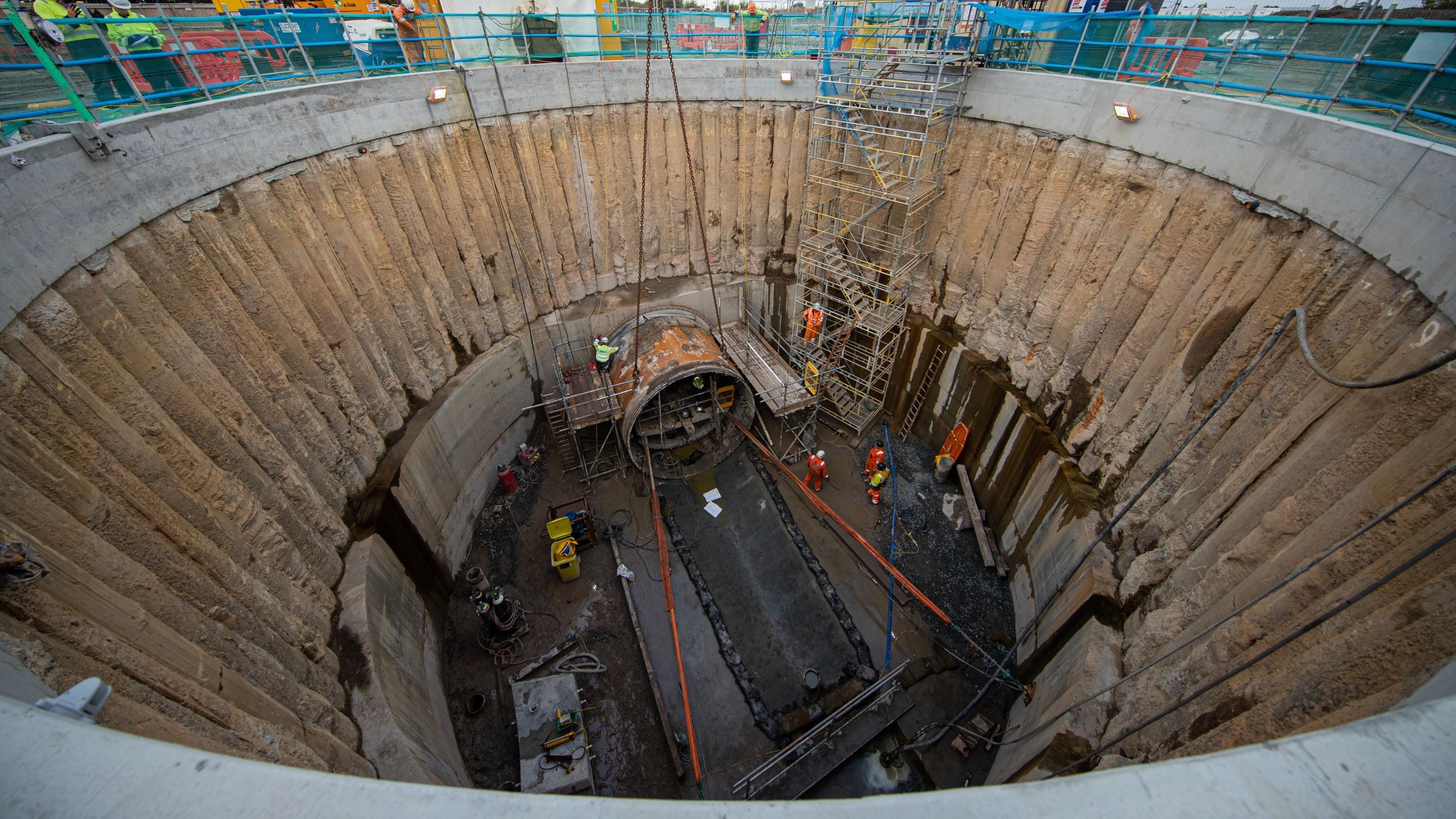 Gas pipeline shaft Construction workers operate inside a deep circular excavation site with scaffolding.