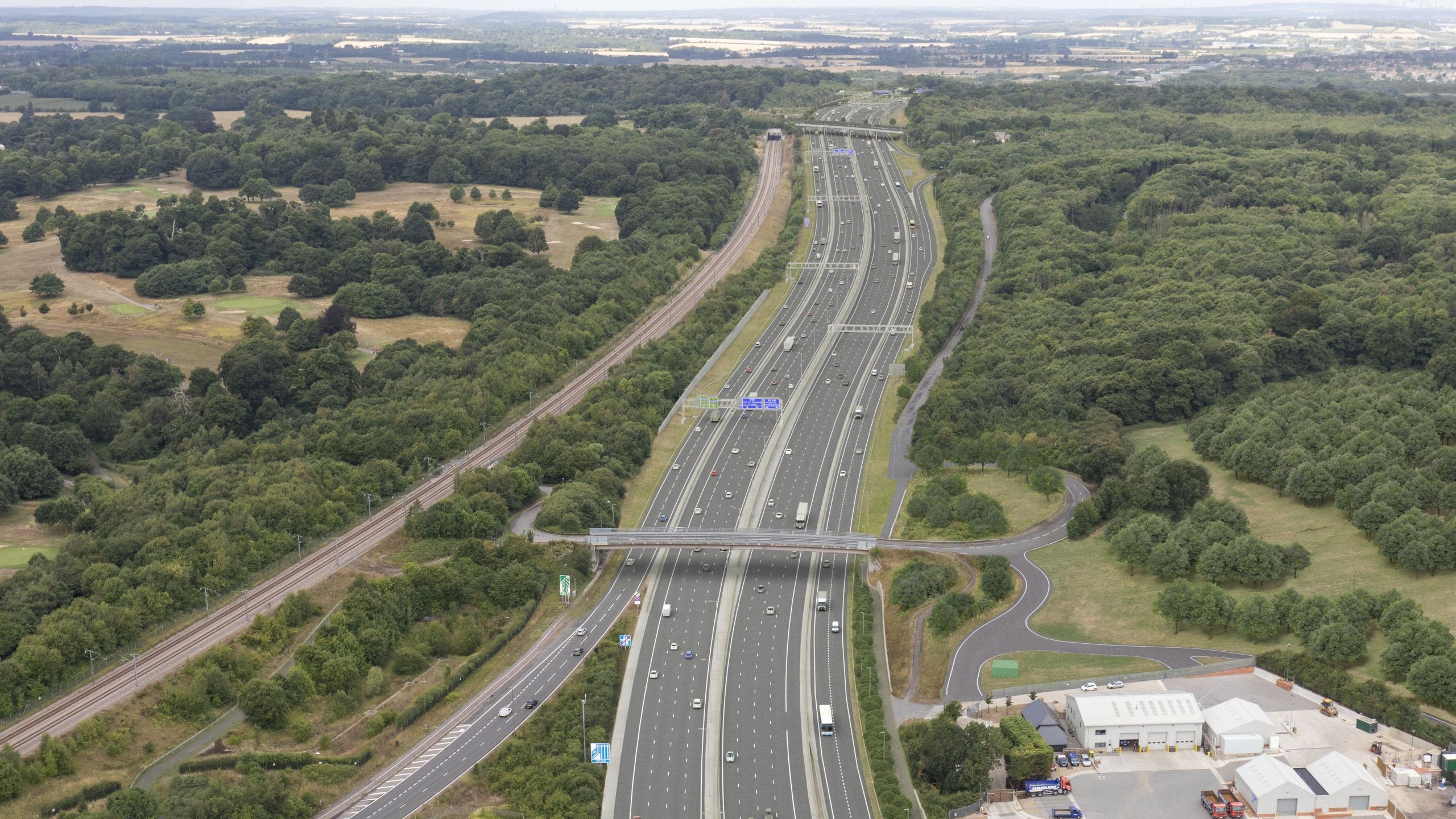 Aerial view of a highway surrounded by dense green forests and adjacent railway tracks.