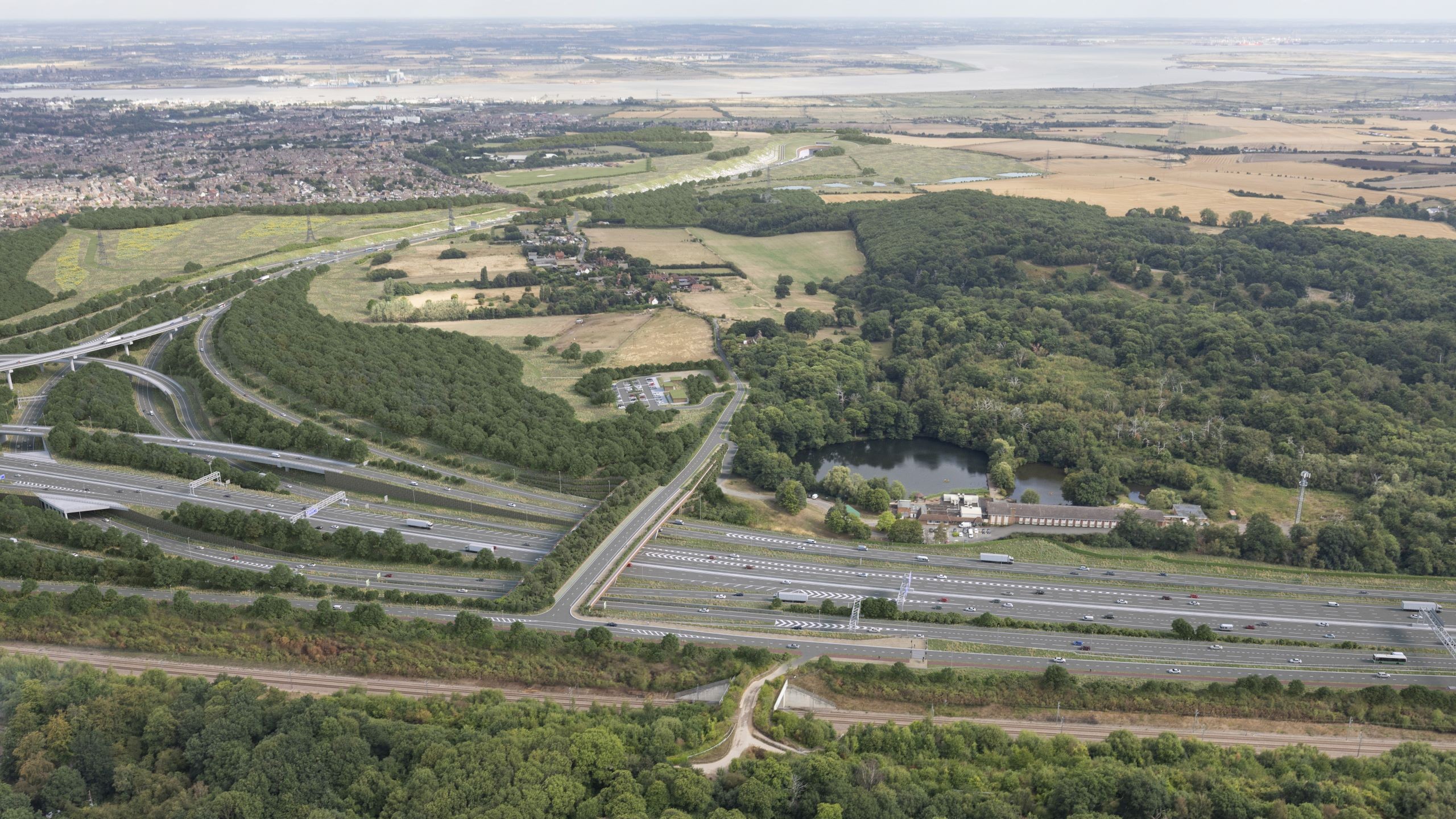Aerial view of a highway interchange surrounded by green fields, forests, and distant town.