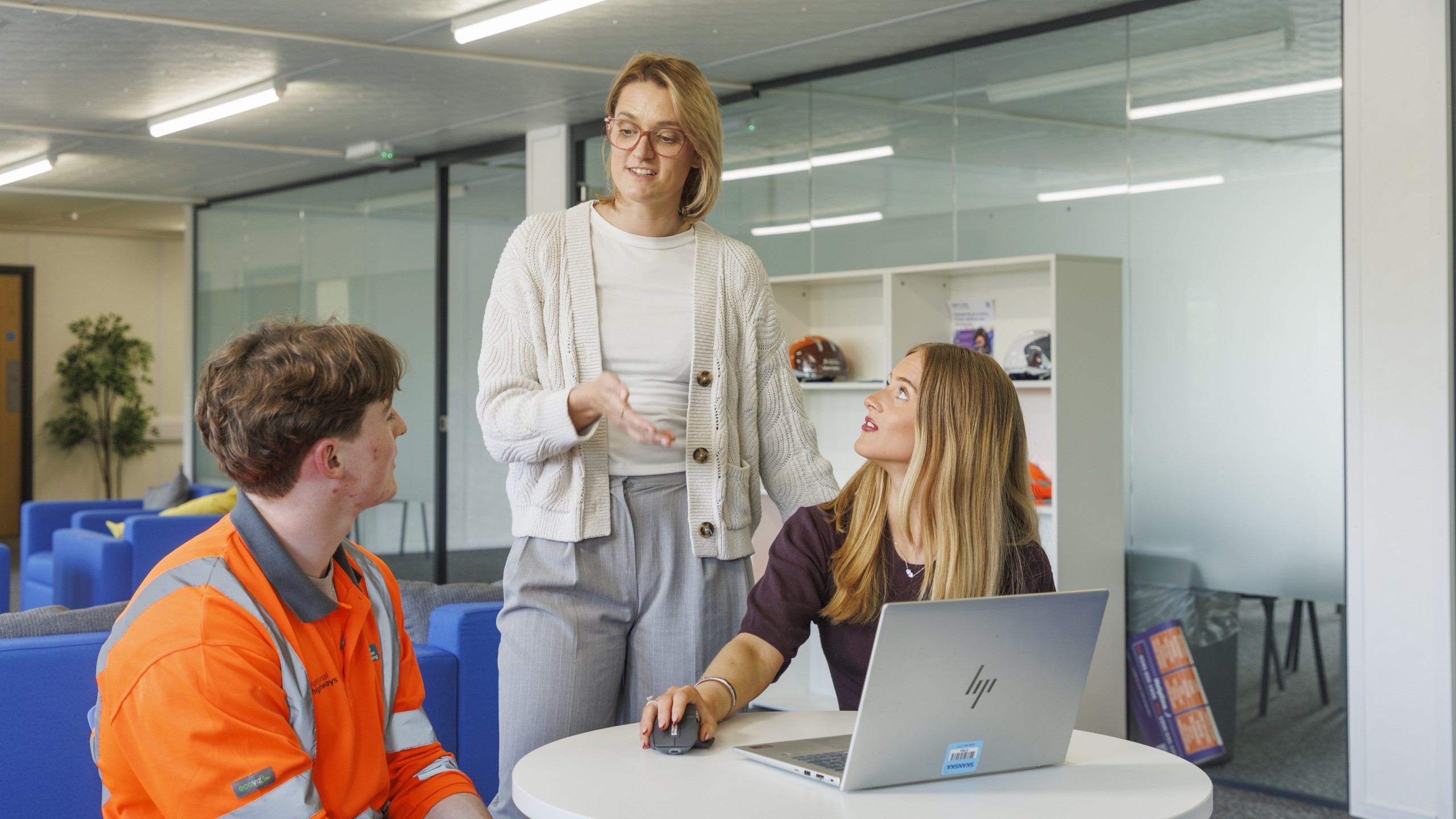 Three professionals discussing work around a laptop in a modern office space.