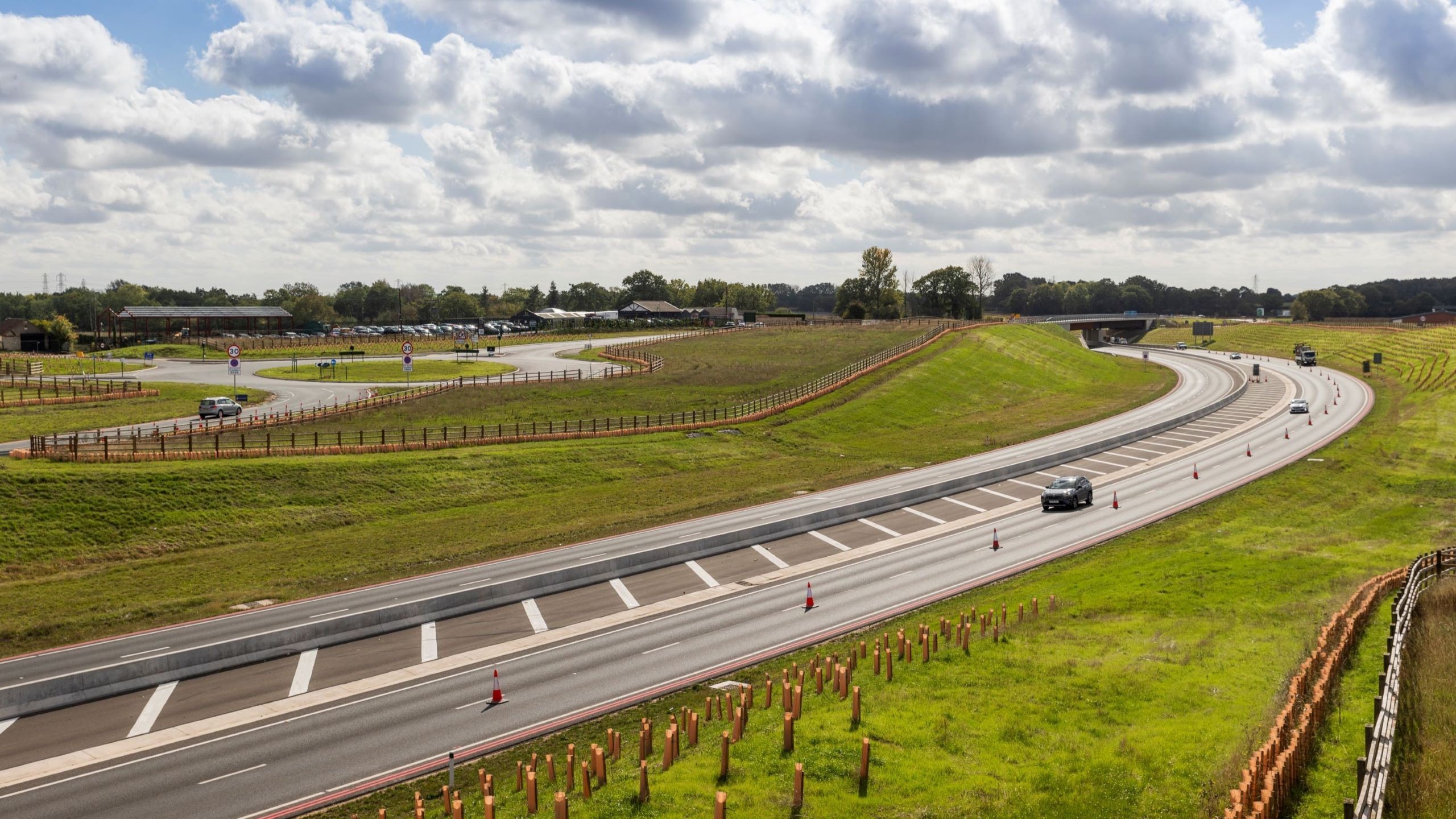Scenic Highway with Gentle Curves and Green Landscape View A winding highway with light traffic under a cloudy sky surrounded by green fields.
