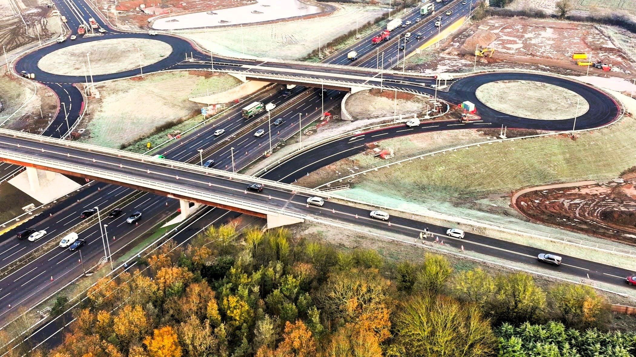 Aerial view of a highway interchange with roundabouts and overpasses surrounded by trees.
