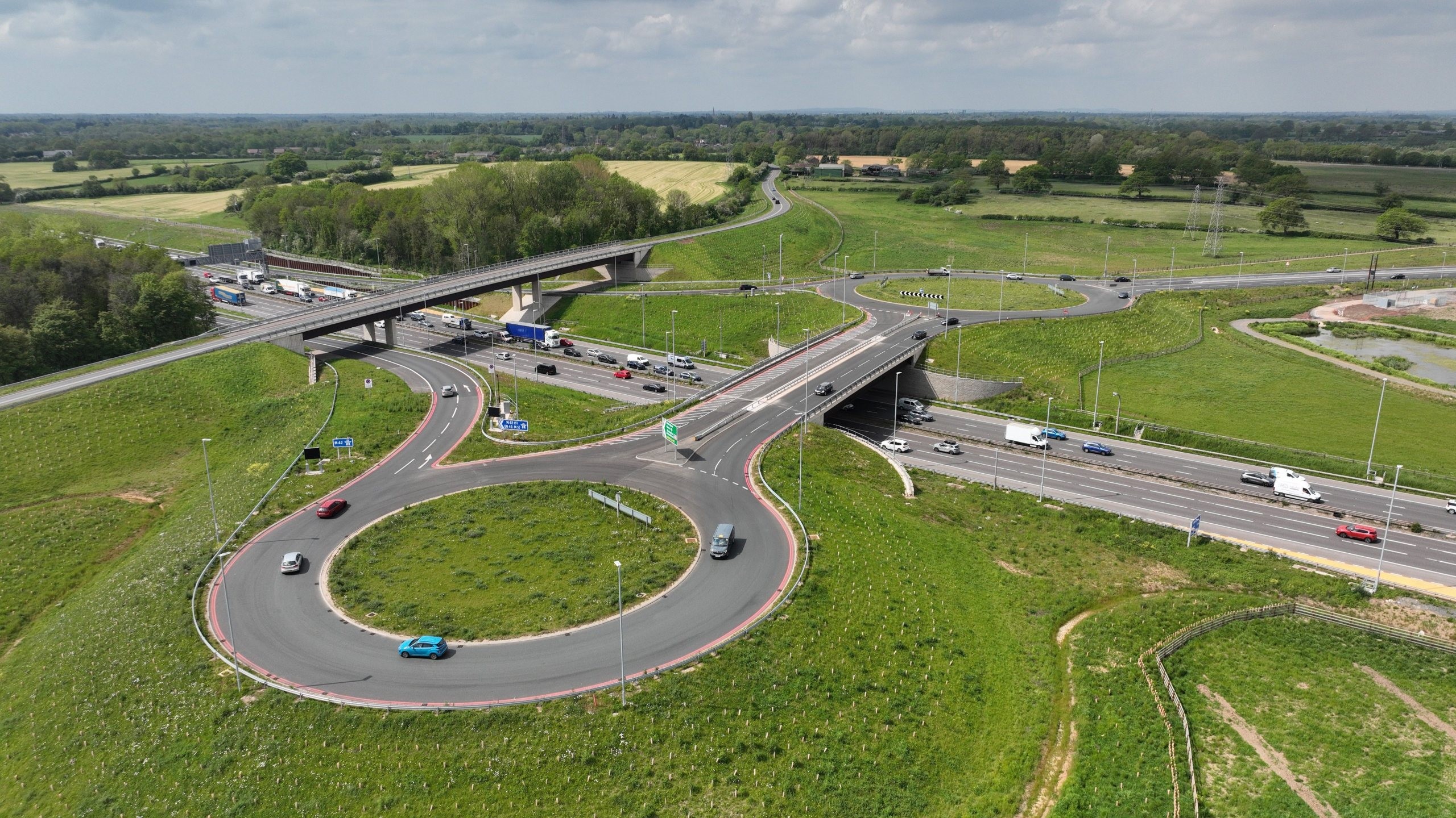 A scenic highway with light traffic winding through green fields under a cloudy sky.
