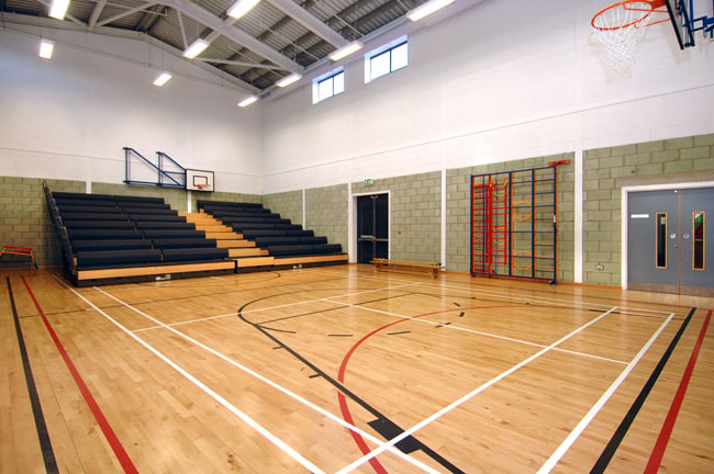 Indoor basketball court with wooden floor, bleachers, and basketball hoops.