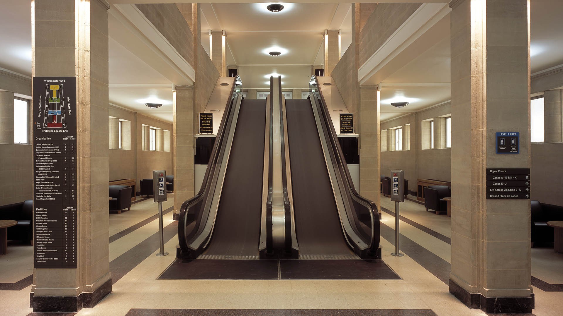 Elegant escalators in a spacious, modern interior with beige stone walls and ample lighting.