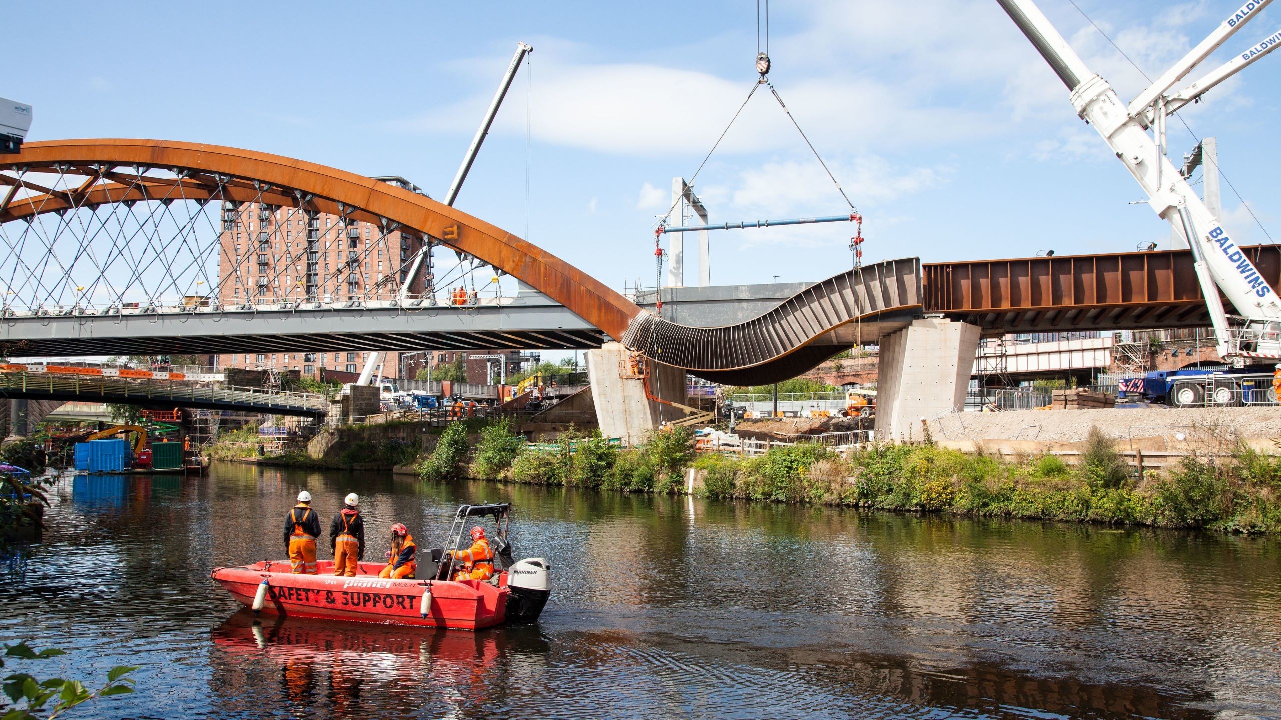 Construction workers on a boat near a partially built arched bridge over a river.