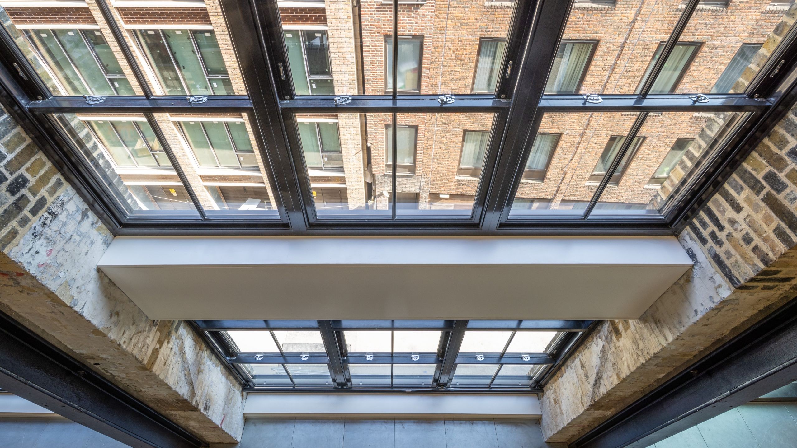 Modern industrial loft with large steel-framed windows view View looking up at modern glass ceiling with brick walls and metal framing in building.