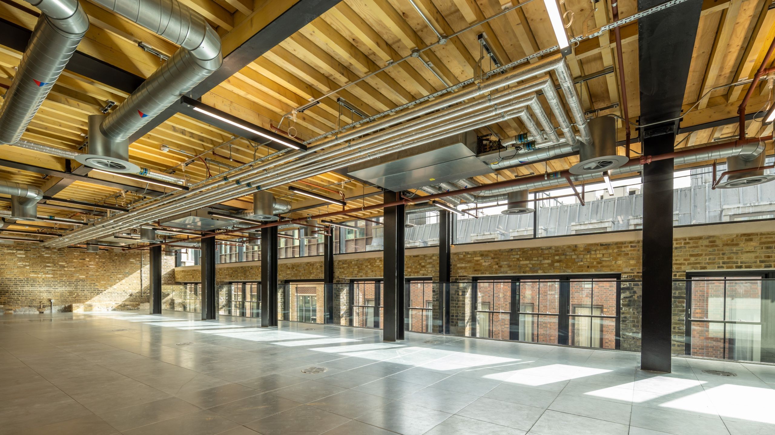 Spacious modern industrial office interior with exposed ceiling pipes and large windows.