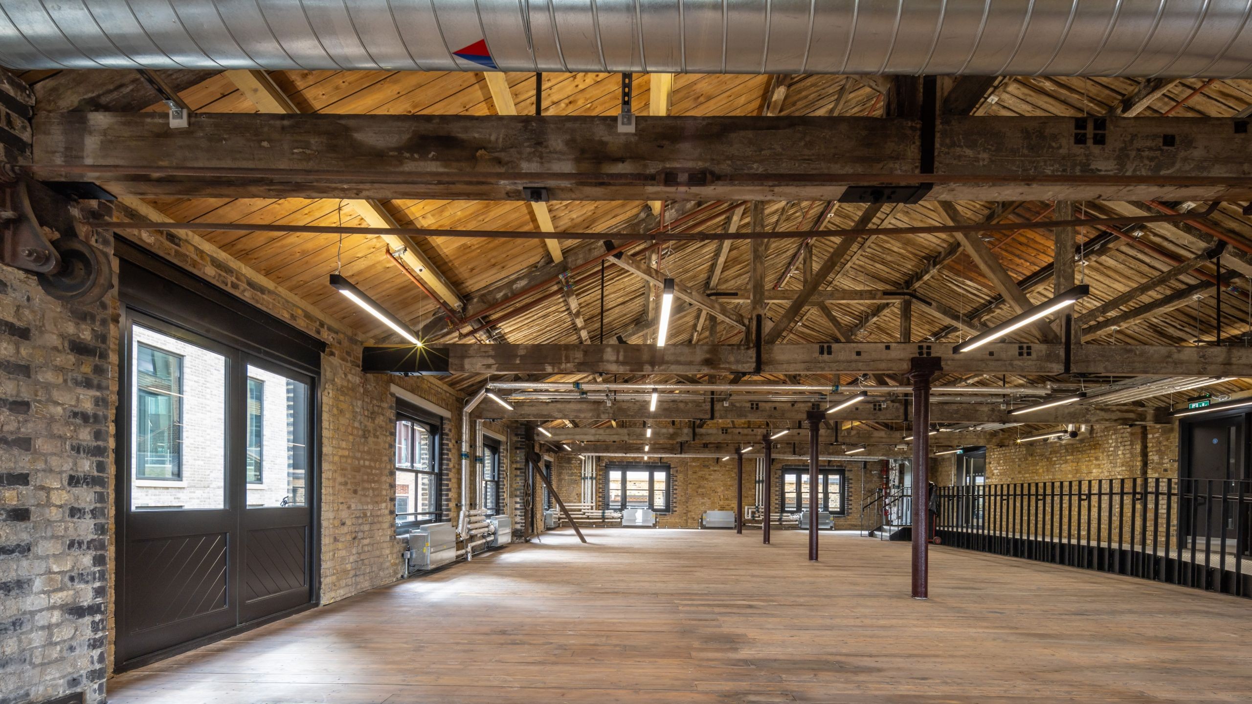 Spacious industrial loft with wooden beams, exposed brick walls, and large windows.