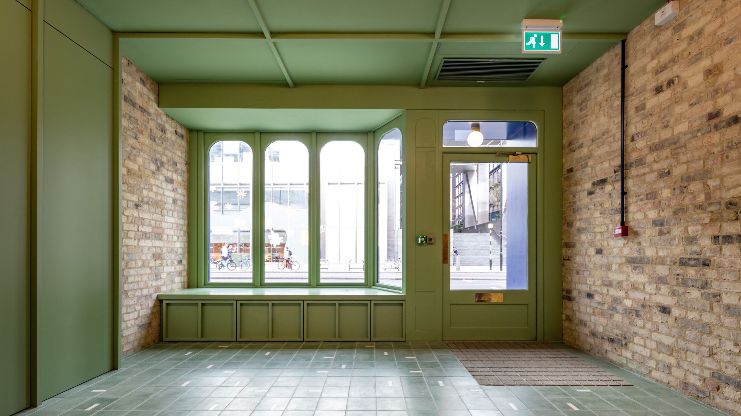 Empty modern interior with green walls, large windows, and exposed brick accents.