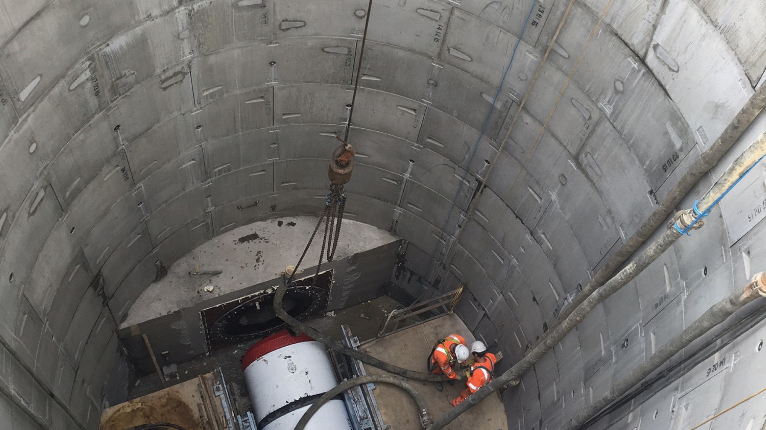 Construction workers operating machinery inside a deep concrete tunnel shaft.