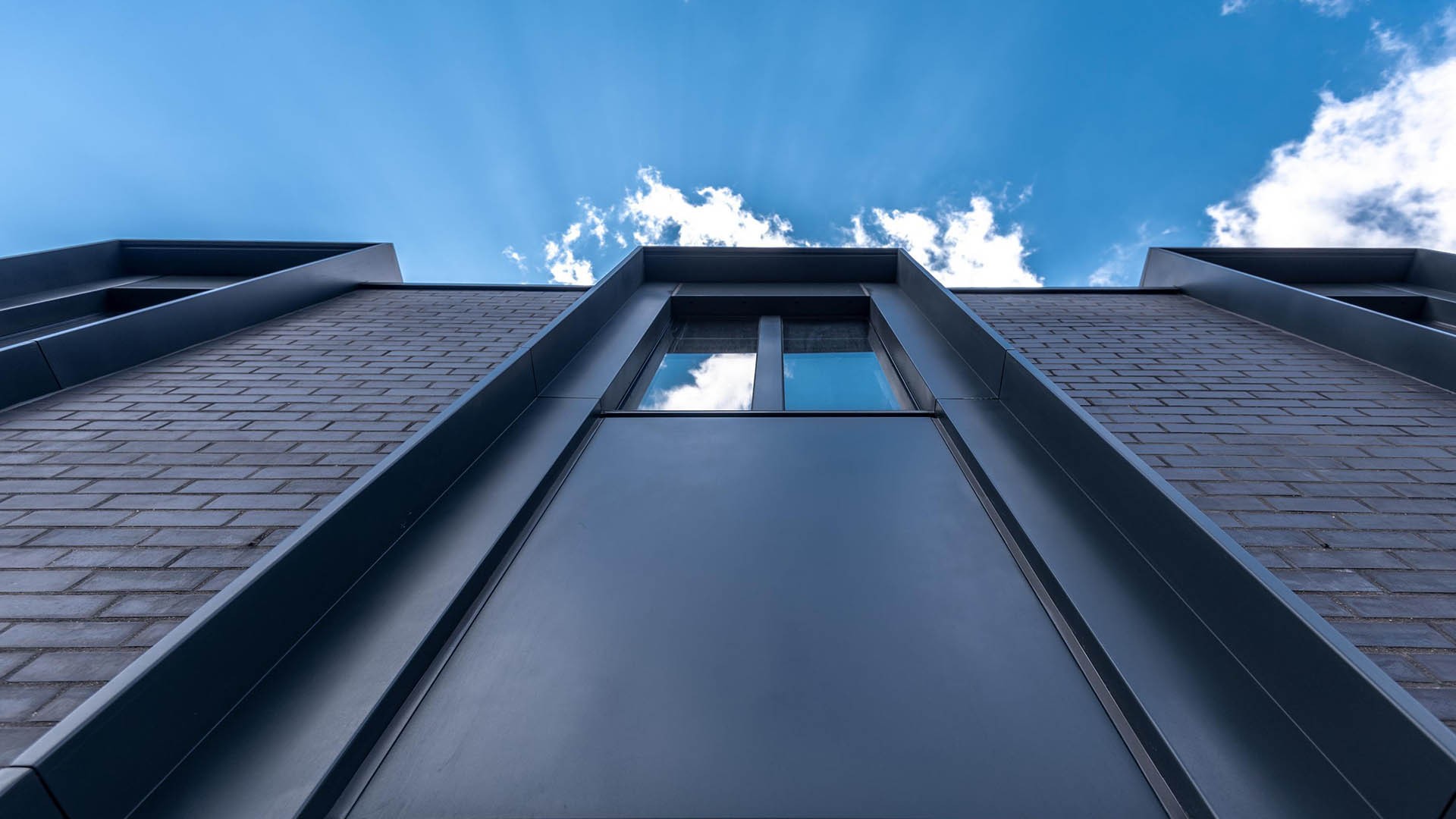 The Earnshaw Building Low-angle view of a modern building facade against a bright blue sky with scattered clouds.