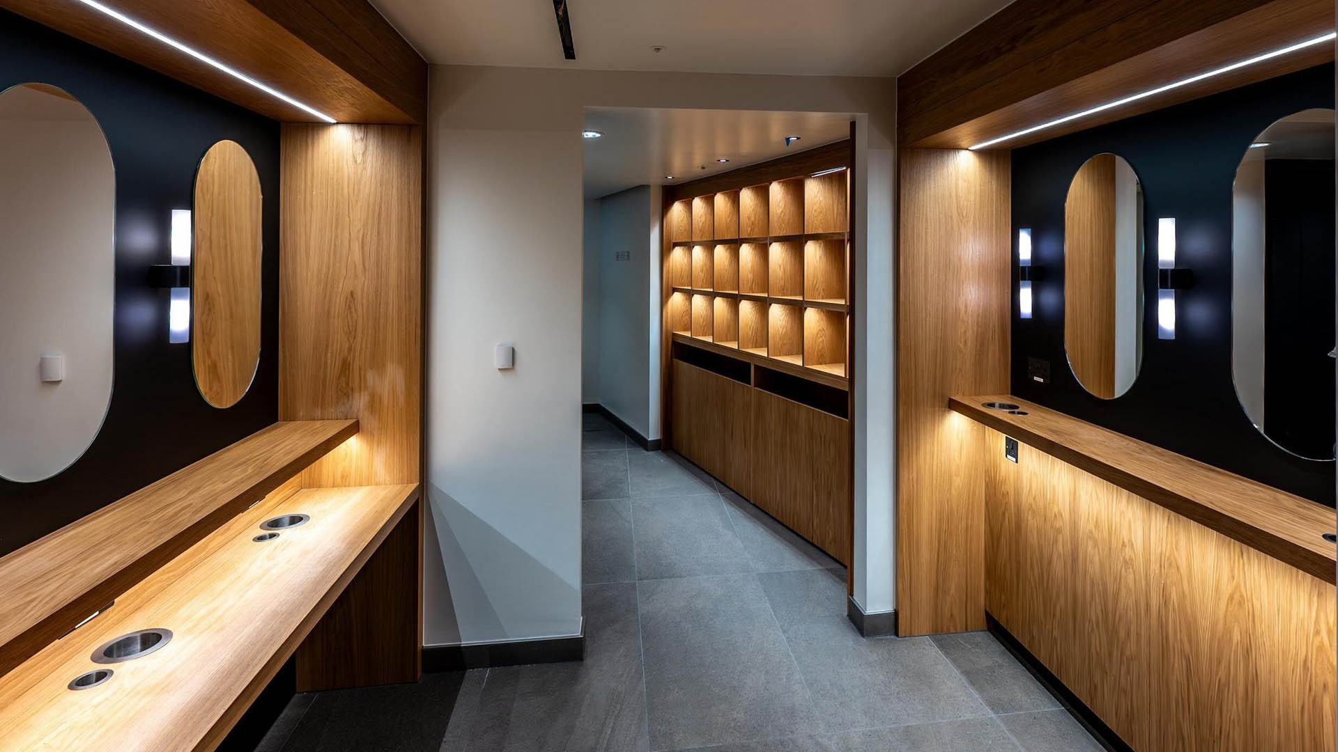 Modern restroom with wooden accents, large mirrors, and stylish lighting fixtures.