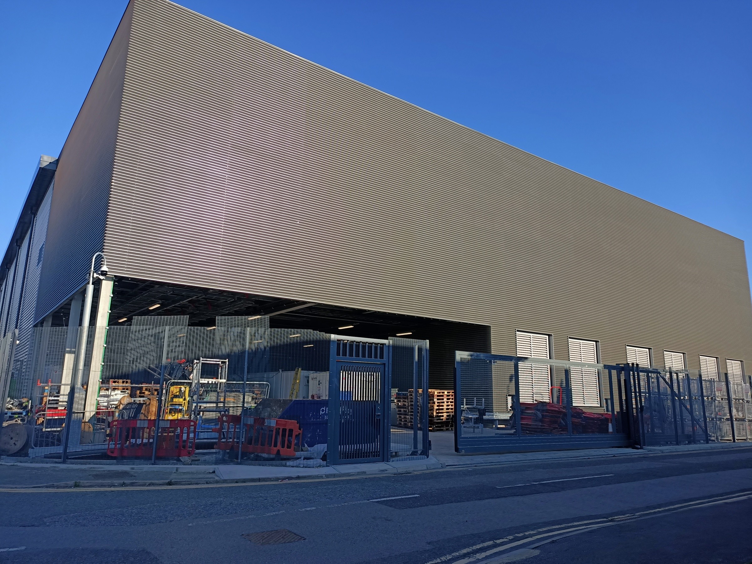 Virtus 11 Modern industrial warehouse with metal siding and fenced outdoor storage area under clear sky.