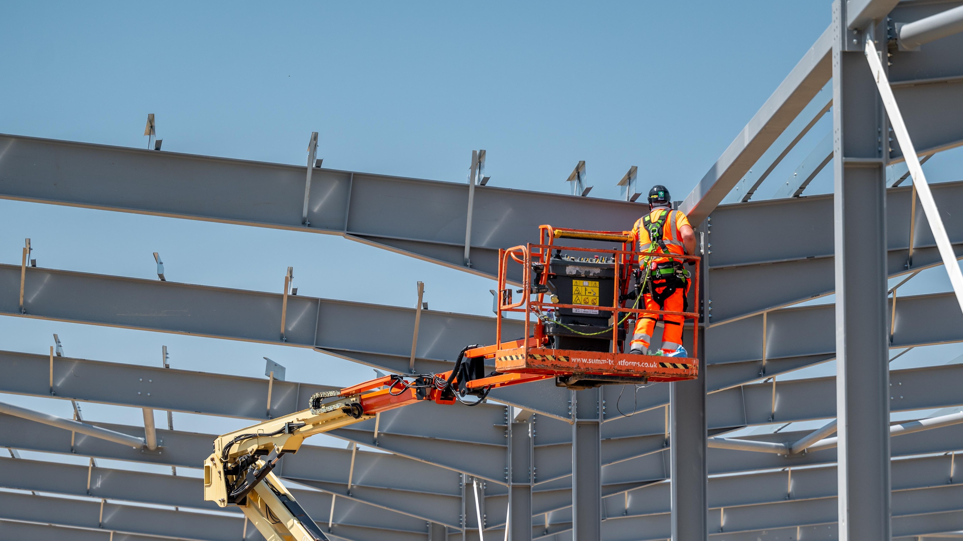 Construction worker on elevated platform inspecting steel beams Construction worker in safety gear on a boom lift working on a steel building frame.