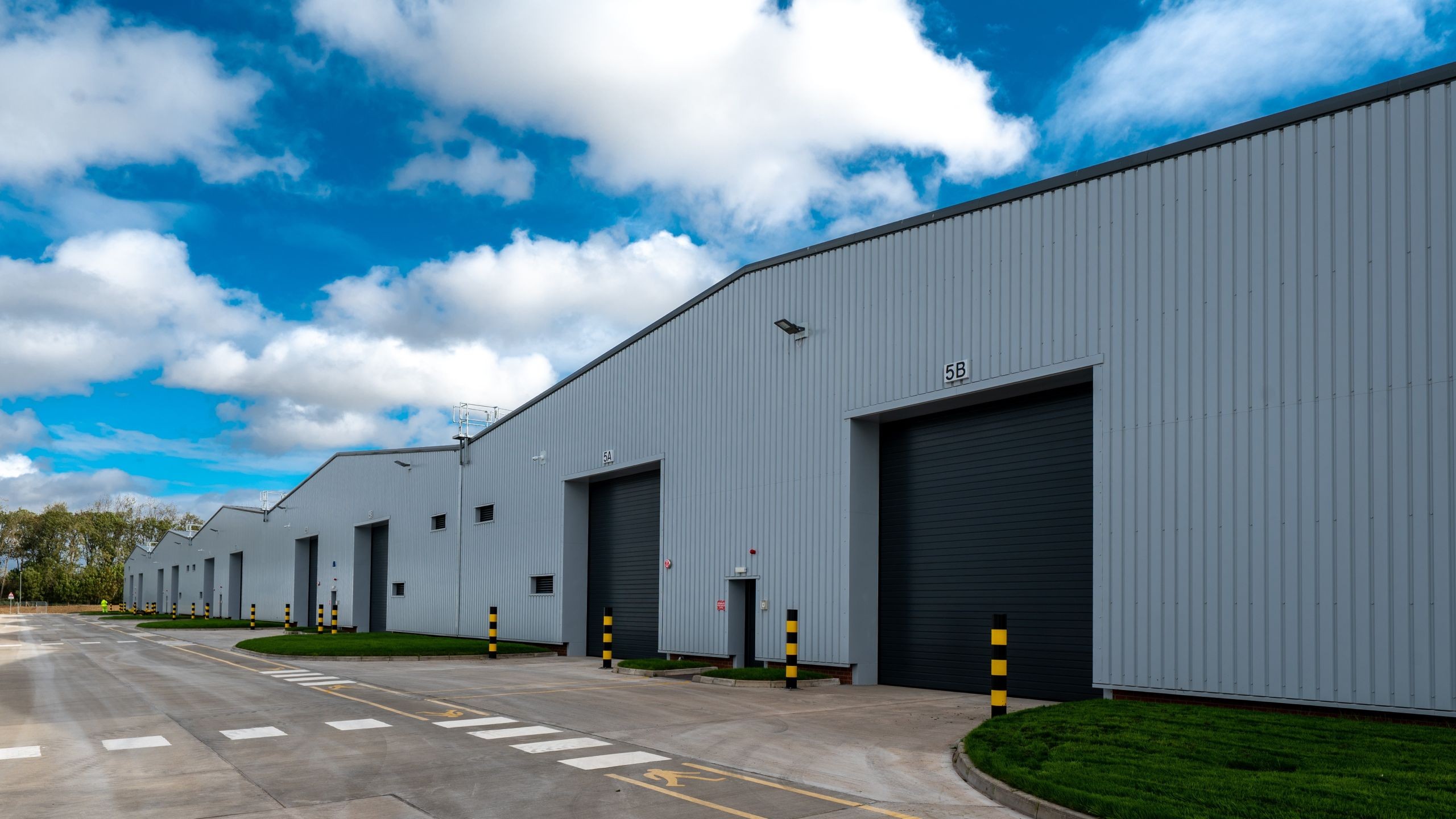 The Vehicle Storage Support Programme (VSSP) at Ashchurch, Tewkesbury Industrial warehouse buildings with large doors along a wide concrete road under a cloudy sky.