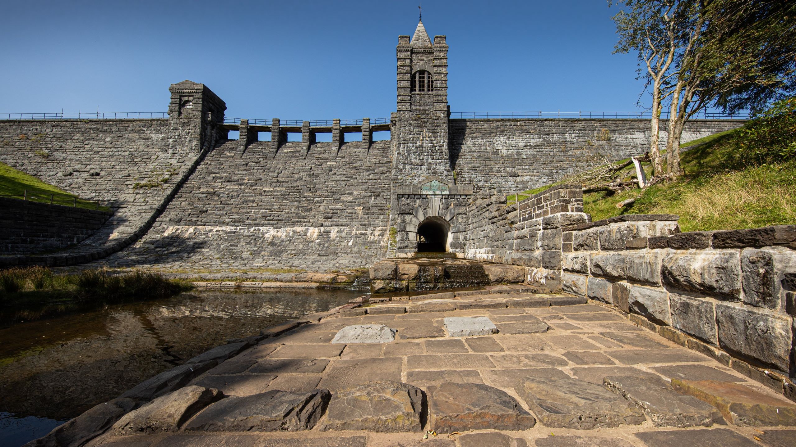 Stone dam with a central tower and clear blue sky in a sunny outdoor setting.