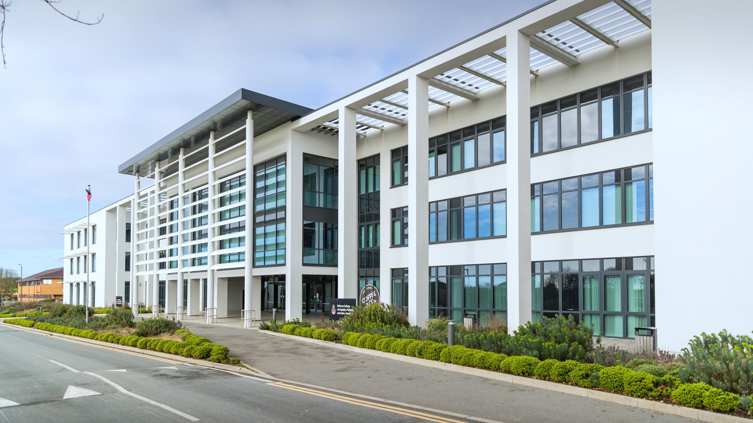 Modern Office Building Exterior with Glass Windows and Columns Modern white office building with large windows and landscaped greenery outside.