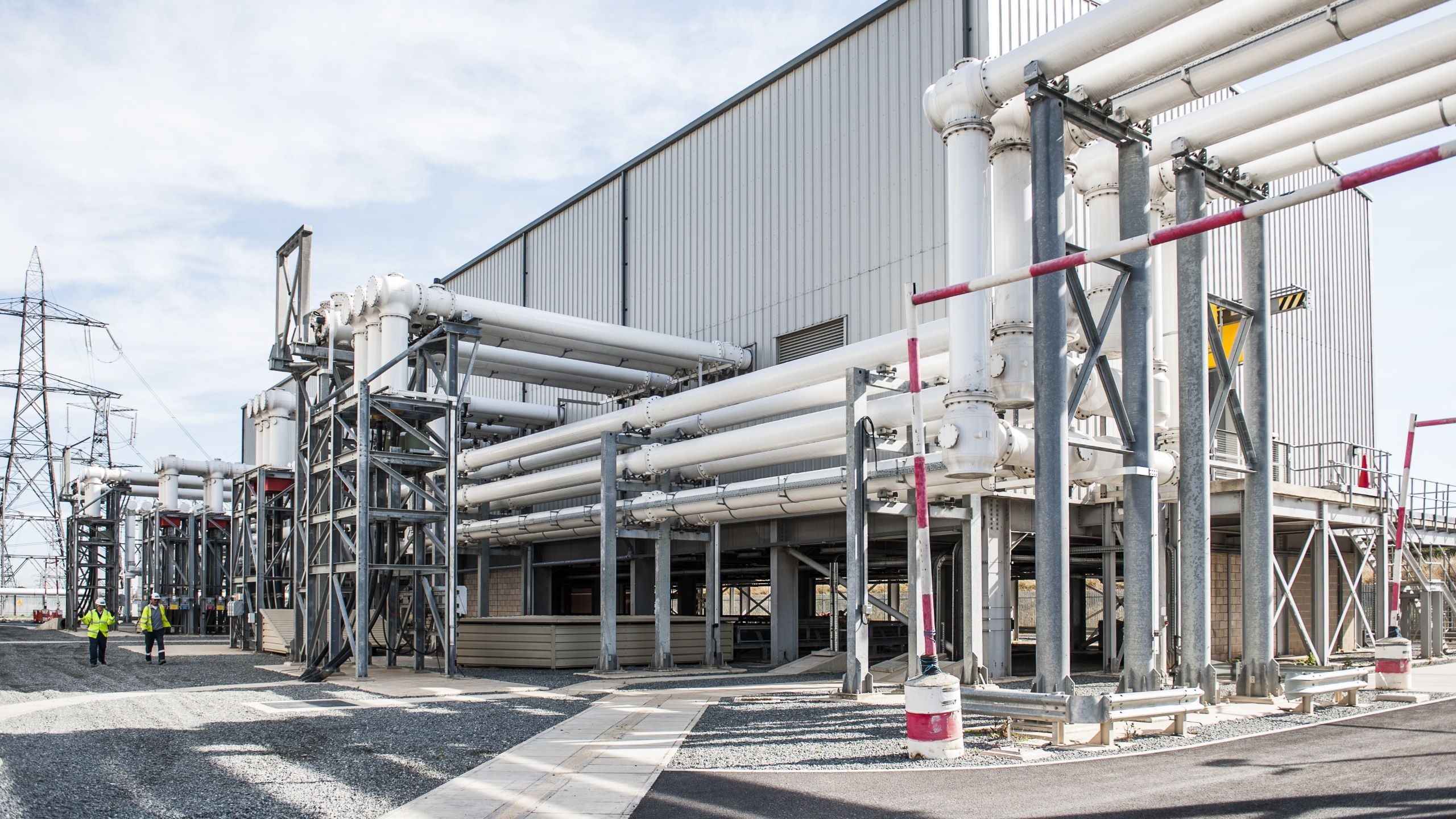Industrial facility with large white pipelines and workers Industrial plant with large white pipes and metal framework under a clear sky.