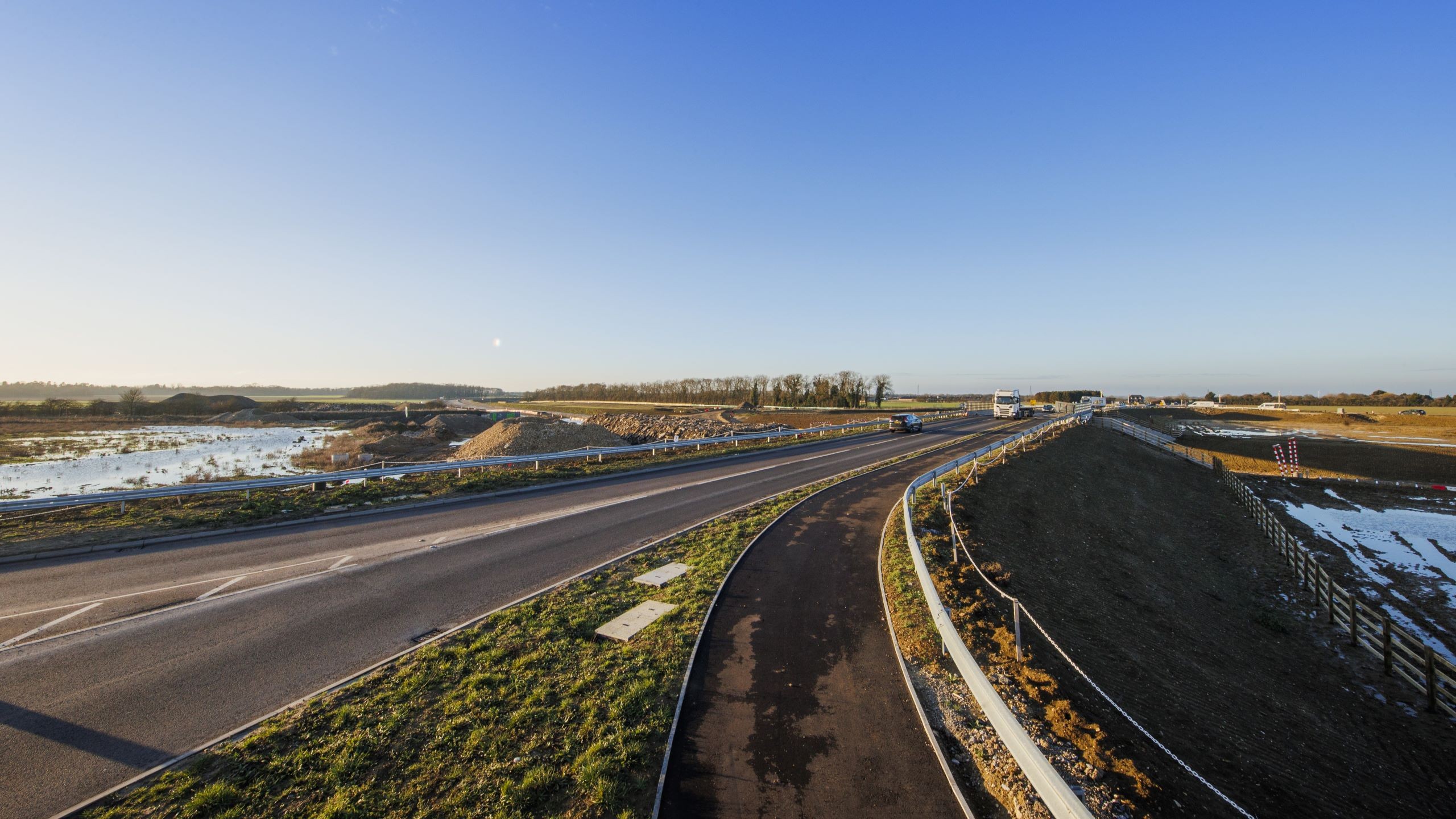 Clear blue sky over a modern highway and adjacent bike path Empty highway with clear sky and surrounding farmland at sunset.