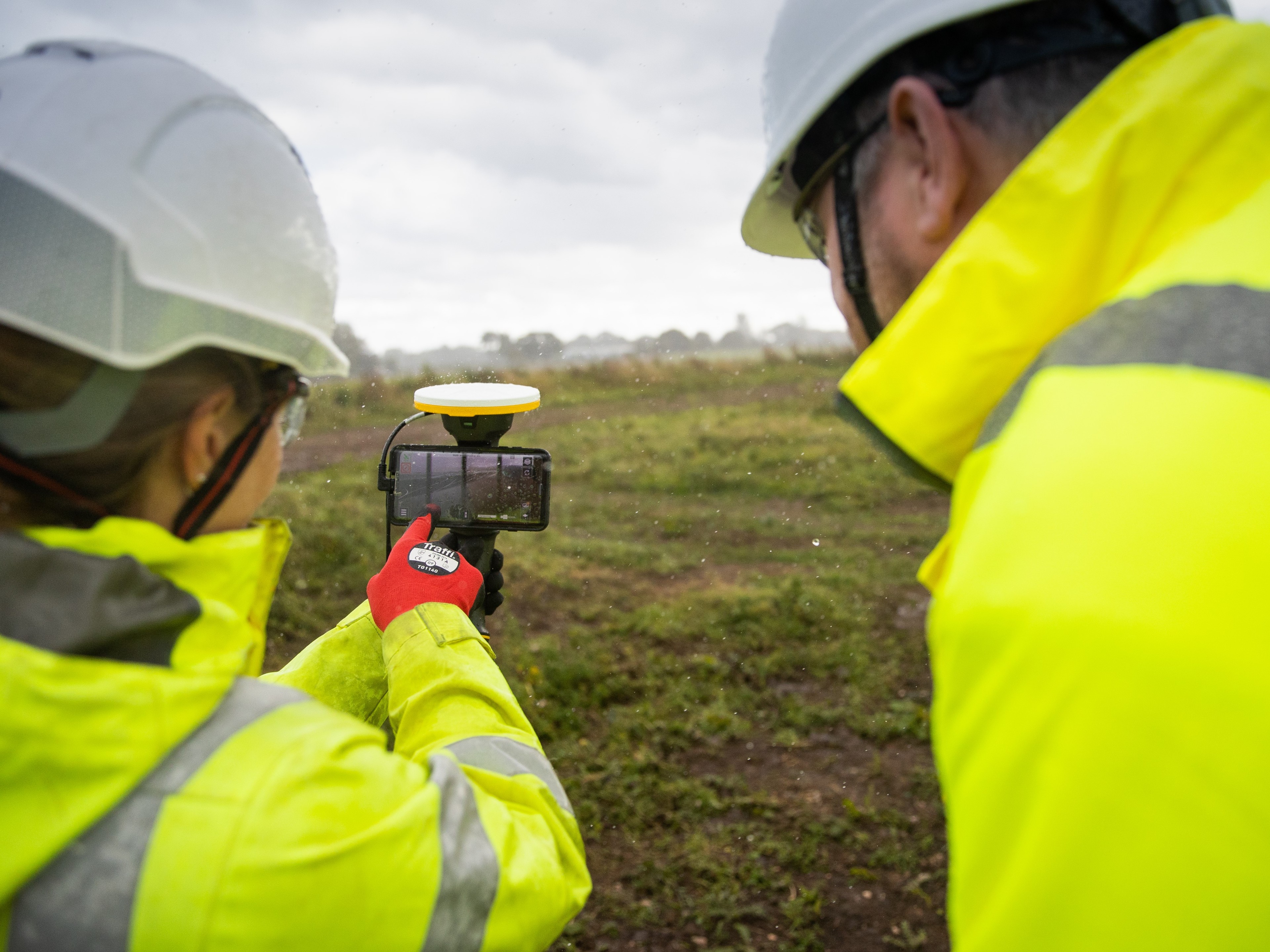 Surveyors Using GPS Equipment for Land Measurement Outdoors Two workers in yellow safety jackets and helmets using surveying equipment outdoors.