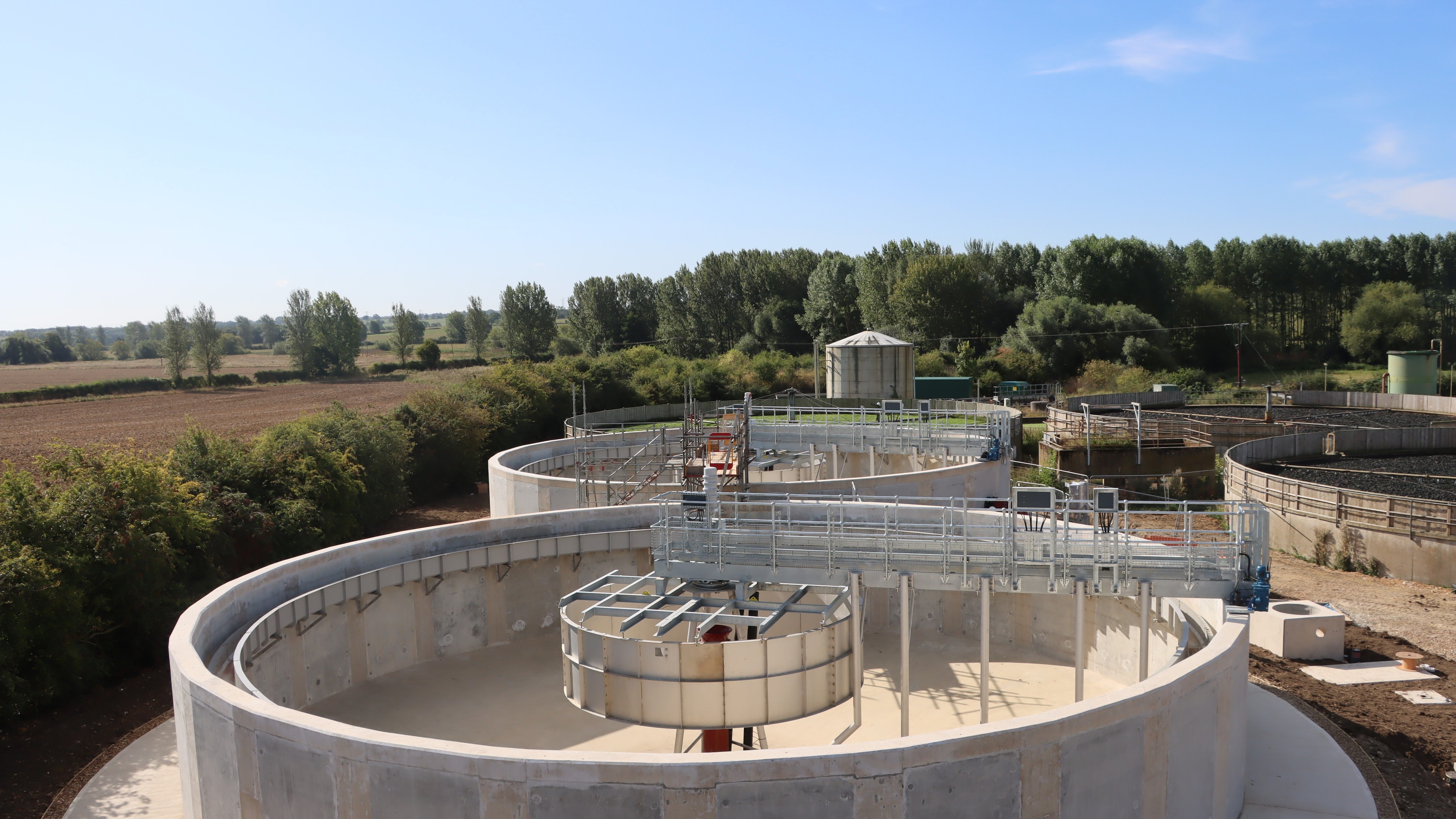 Modern Wastewater Treatment Plant with Clear Skies and Greenery Wastewater treatment plant with large circular sedimentation tanks under clear sky.