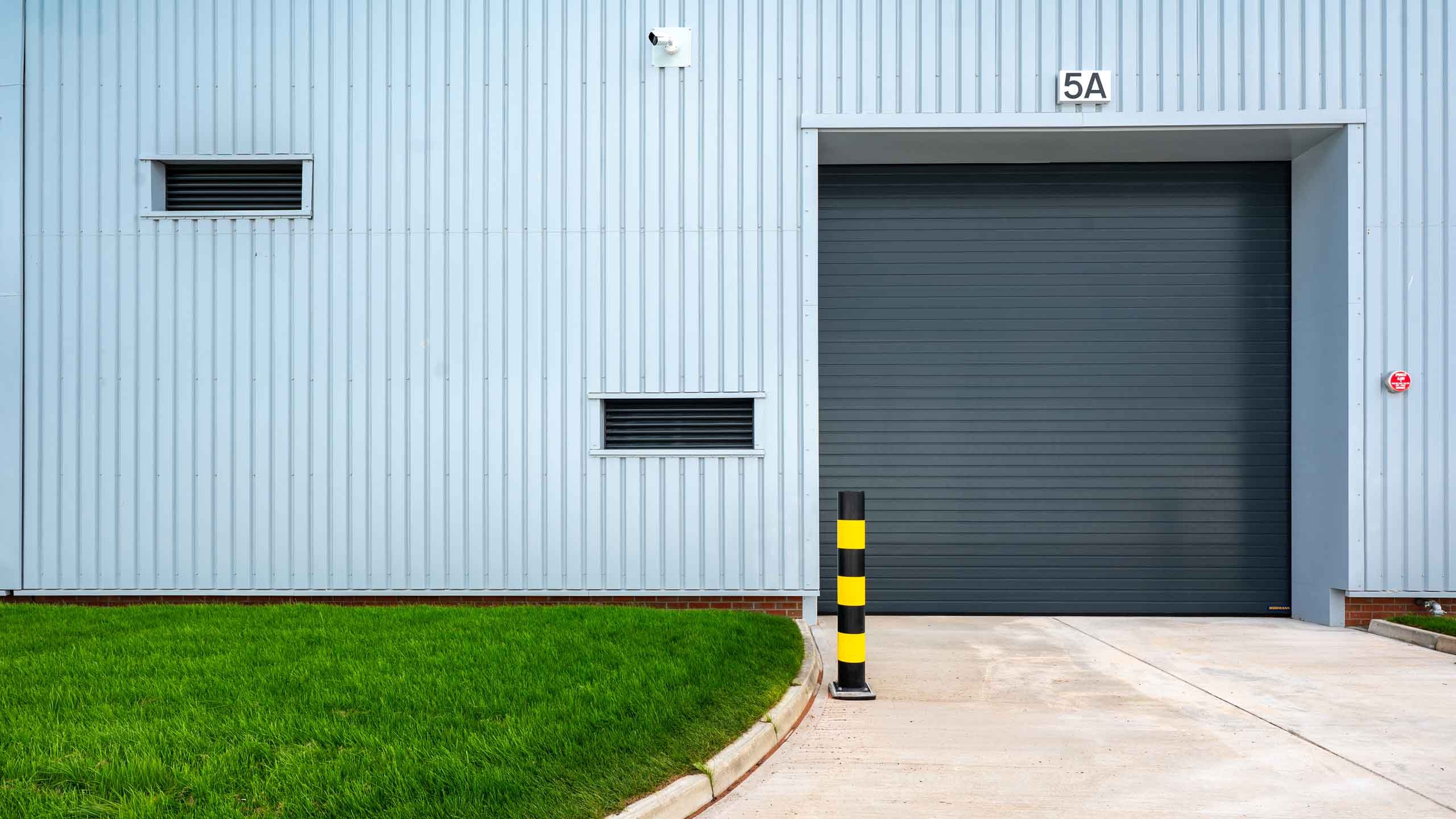 Industrial warehouse entrance with a closed gray roller door and green lawn.